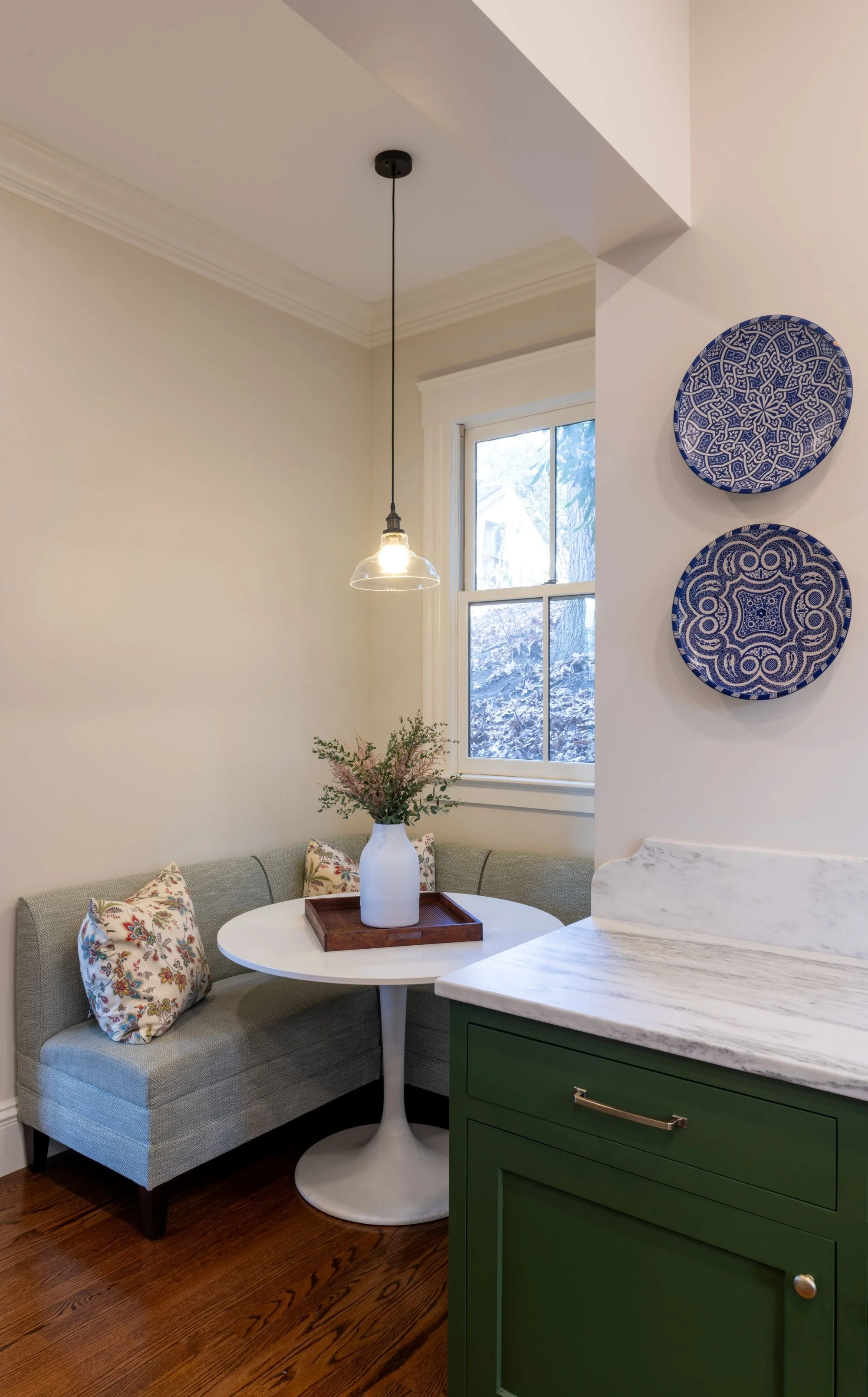 Renovated breakfast nook in an 1846 Victorian home in Newton MA featuring upholstered banquette seating, marble countertop and decorative blue plates