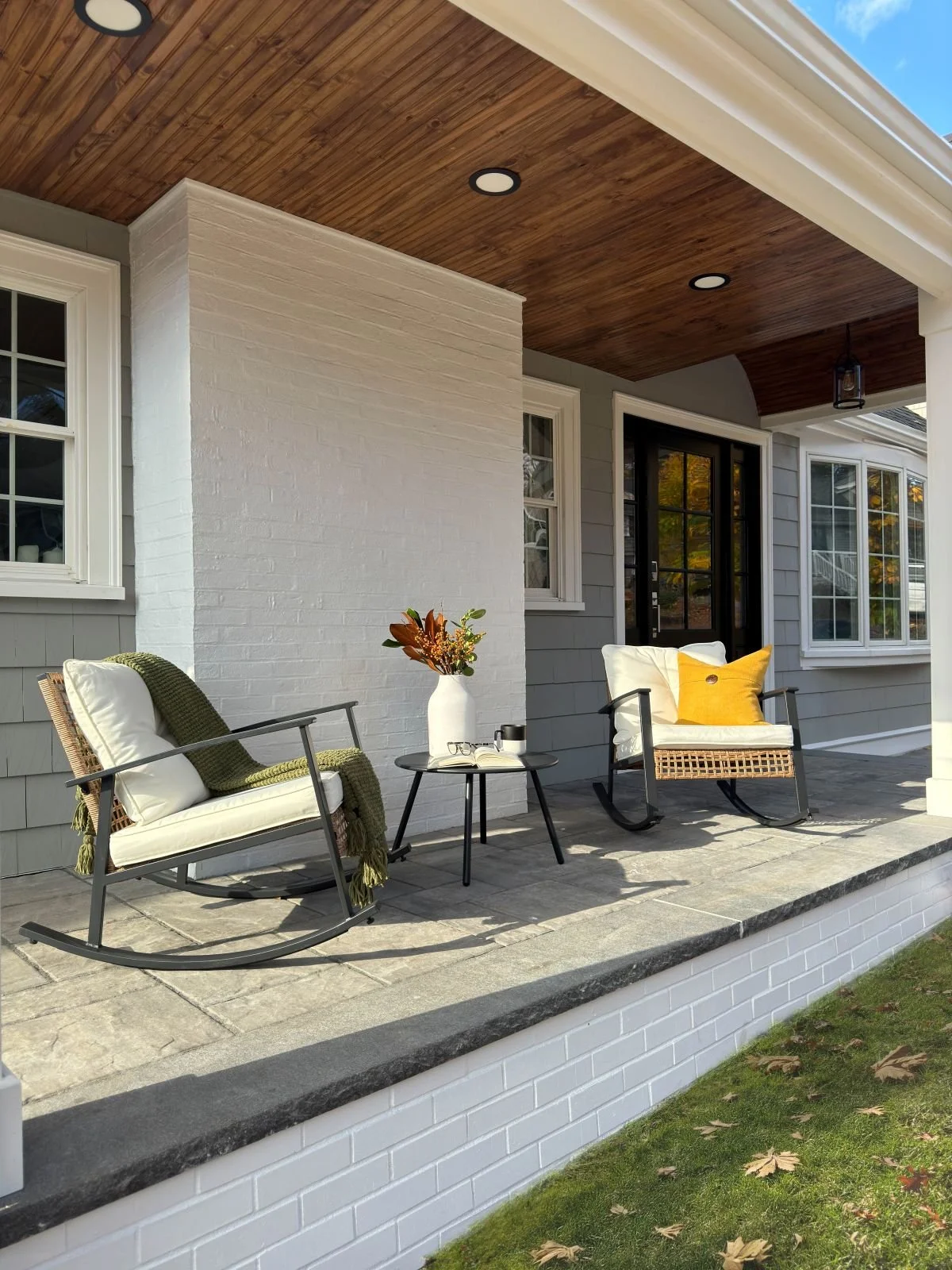 A cozy seating area on the new Melrose porch addition, featuring a material palette of concrete and granite pavers with brick accents. The space is defined by a warm, stained wood ceiling and integrated recessed lighting for a refined outdoor living 