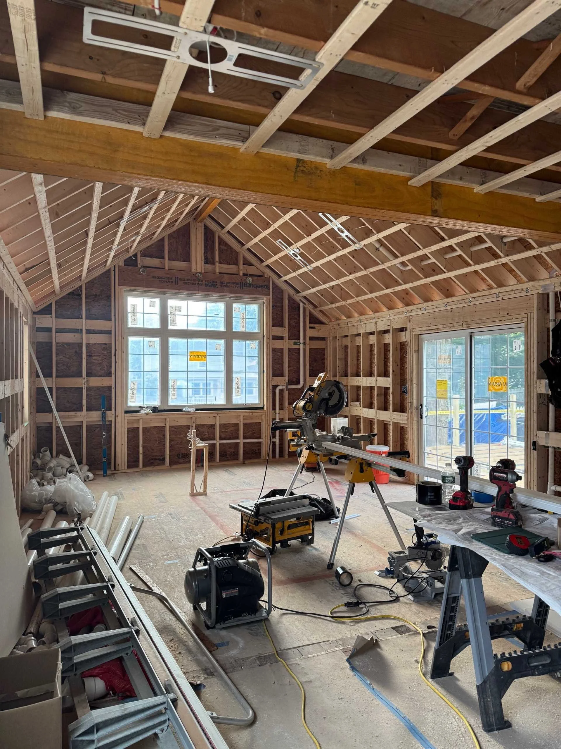 Architectural interior of a newly framed kitchen addition under construction, showcasing structural timber framing and window installation for a residential expansion.