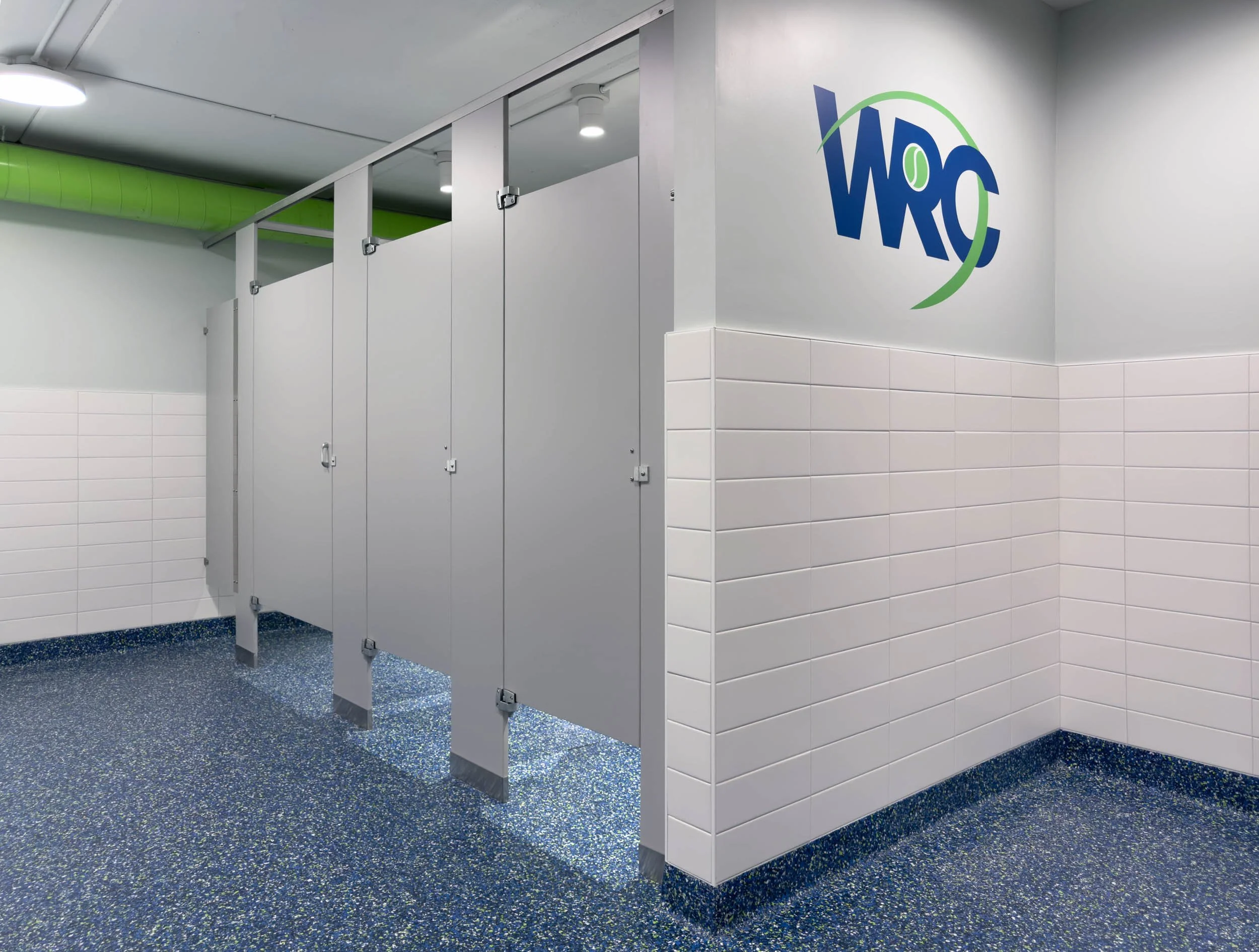 Completed women's locker room toilet stalls with WRC logo and green ductwork in Woburn, MA