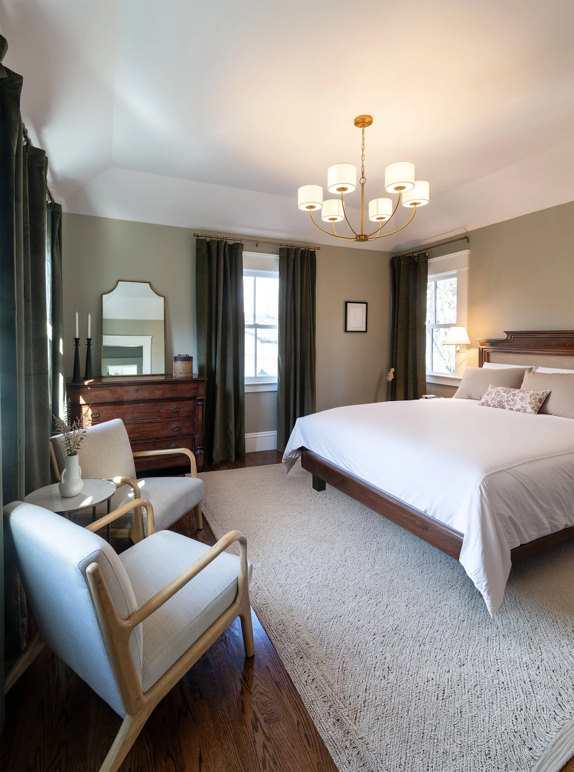 Renovated primary bedroom of an 1846 Victorian home in Newton MA featuring queen bed, brass chandelier, hardwood floors and seating area
