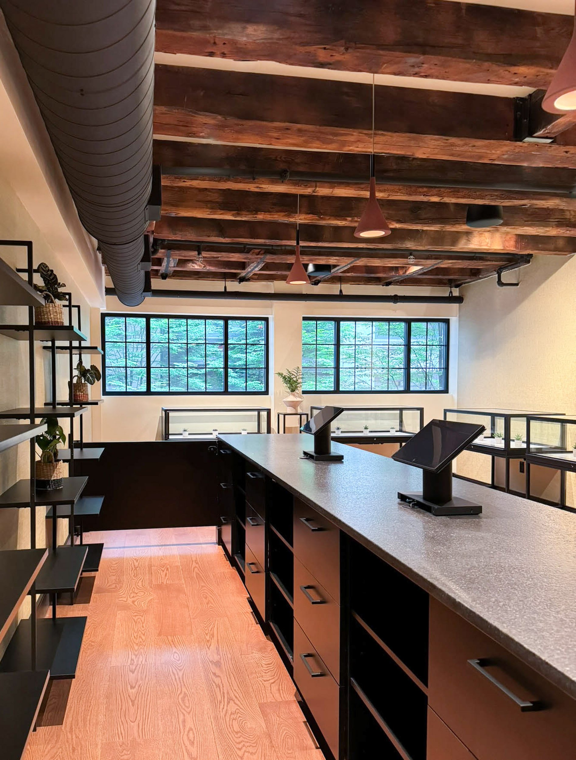 Retail custom cash wrap with drawers and open shelving for equipment and storage with black displays beyond and large horizontal windows under original heavy timber beams.
