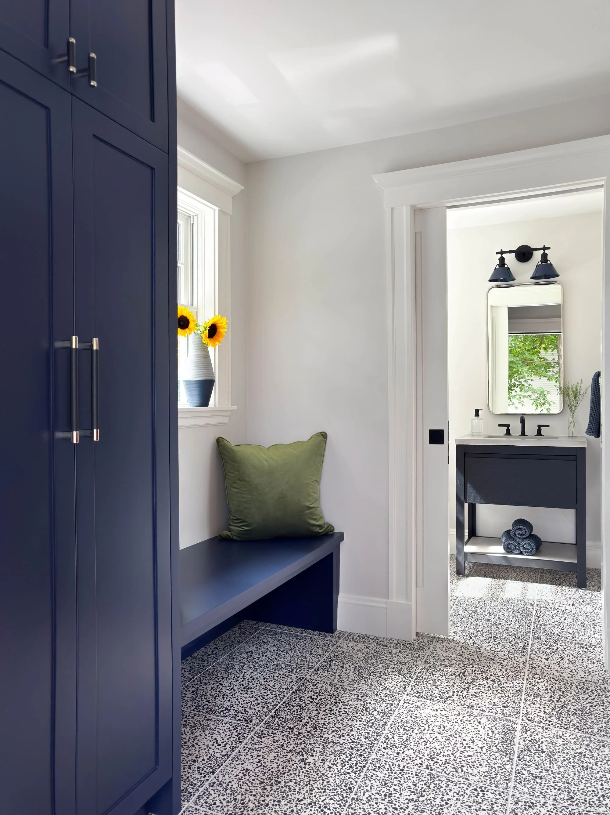mudroom view to connecting powder room featuring custom deep royal blue cabinetry and bench with natural light from backyard windows