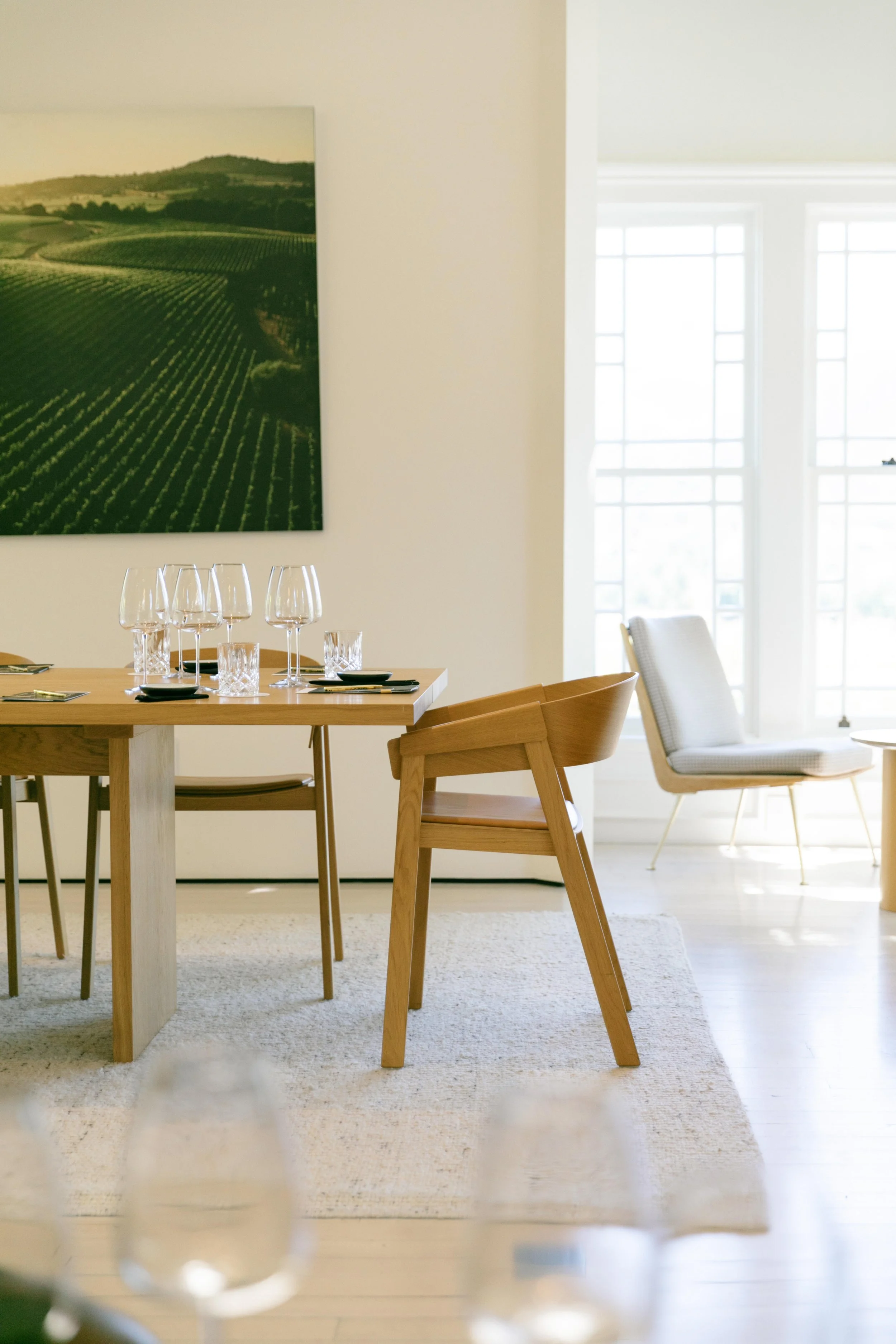 A wine tasting room with a wooden table set with wine glasses and black plates, surrounded by wooden chairs. Wild Zephyr Napa Valley Wine Experience Photographer