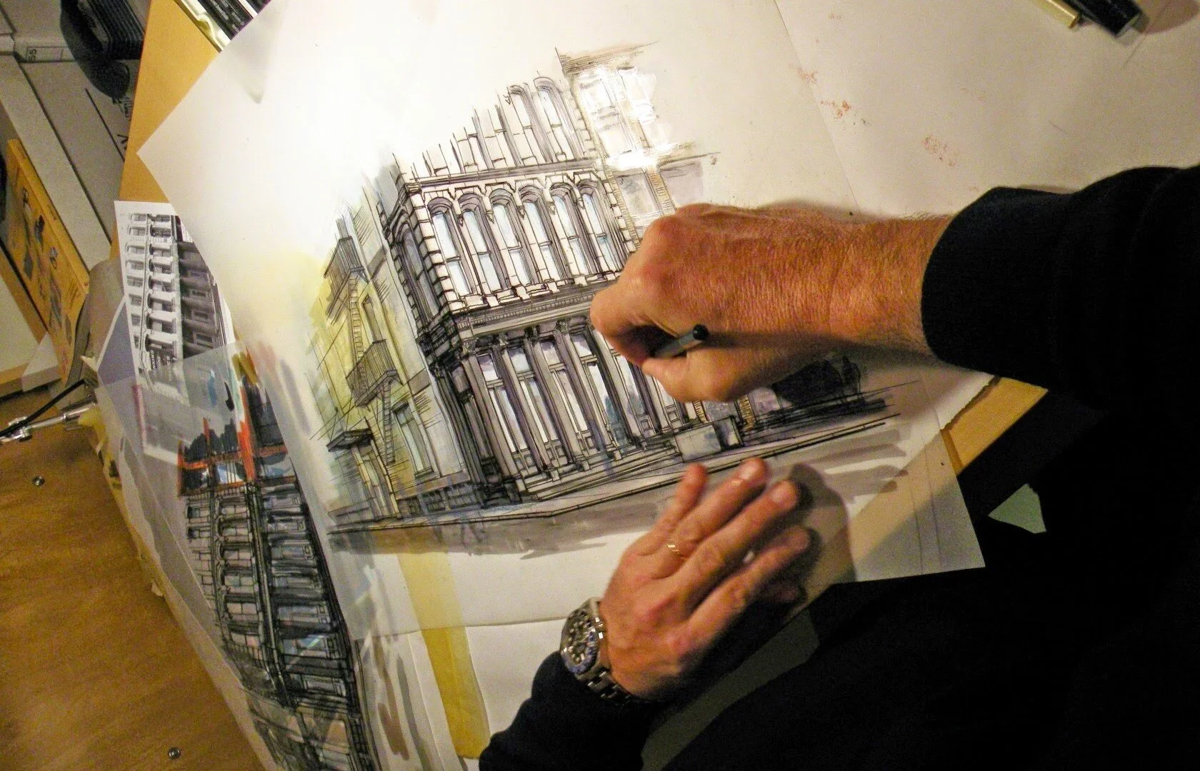 An artist working on an architectural drawing of a building with ornate details and multiple floors, on a large table.