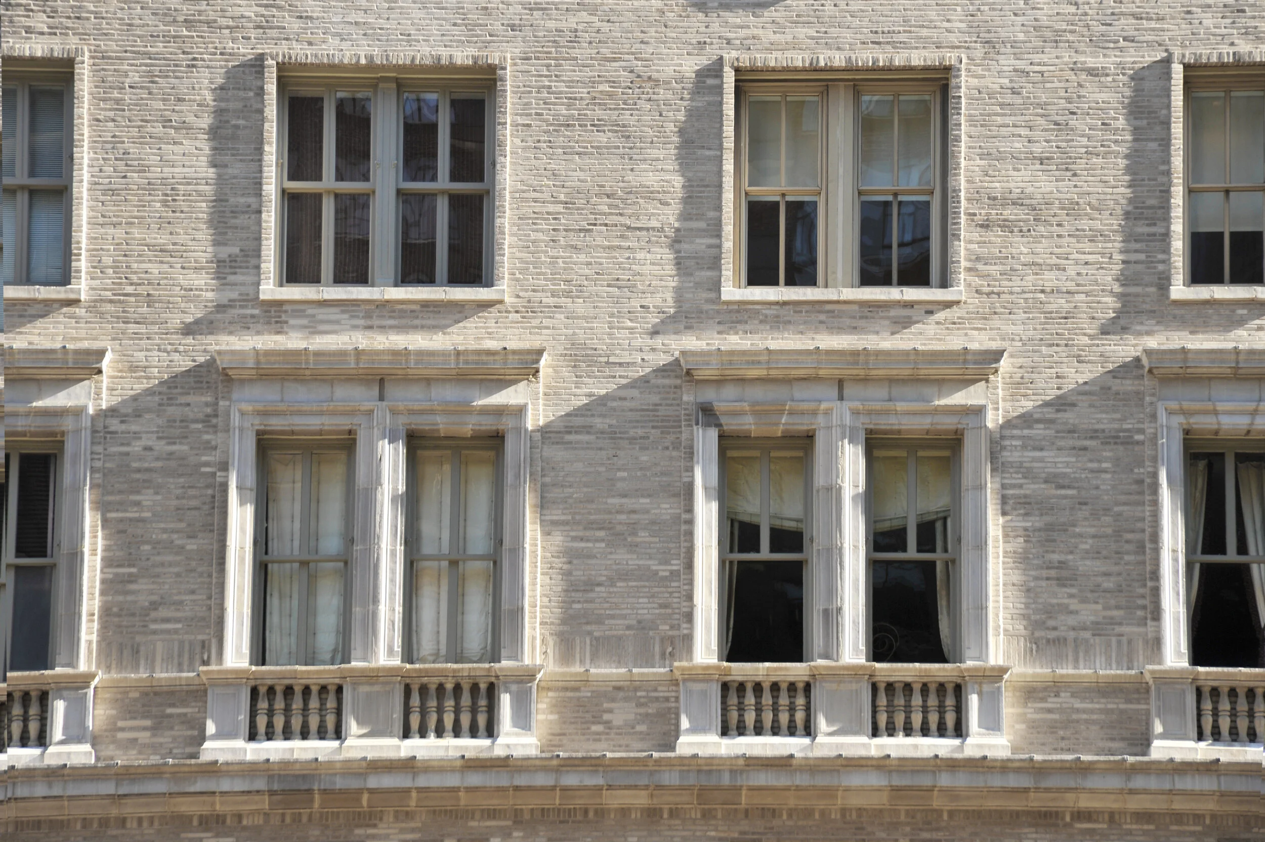 Close-up of a building's brick facade with six windows, three on top and three below, with decorative window frames and shadows.