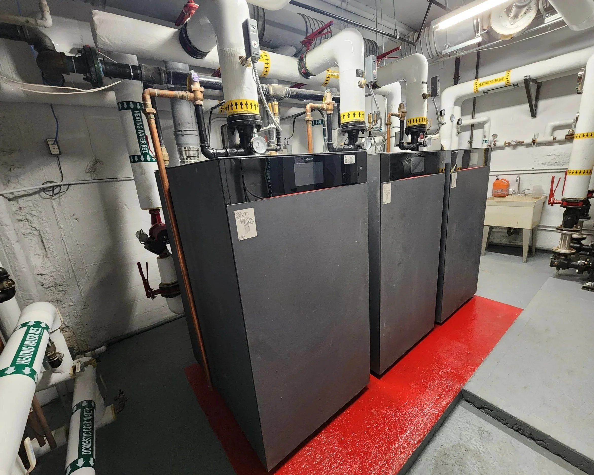 Heating system equipment with several pipes and controls in a mechanical room, mounted on a red platform.