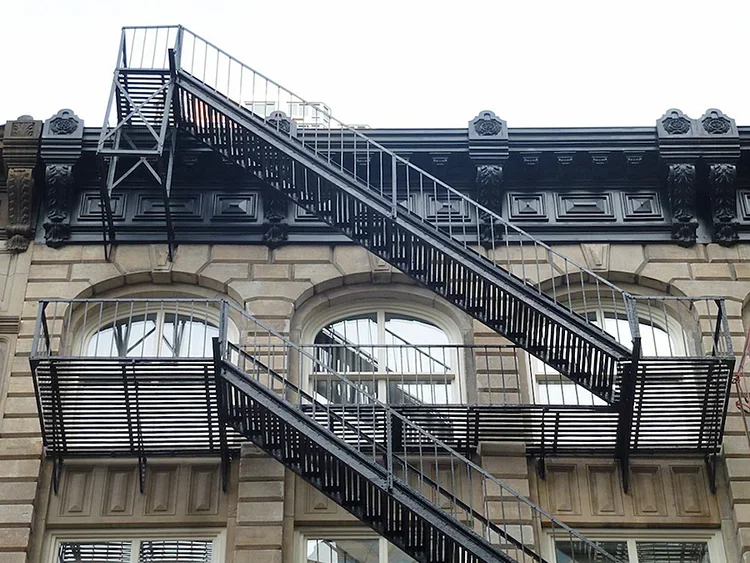 Fire escape stairs on the exterior of a historic brick building with arched windows and decorative black trim.