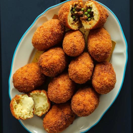 A white platter filled with golden-brown croquettes, with some cut open to reveal creamy and vegetable fillings.
