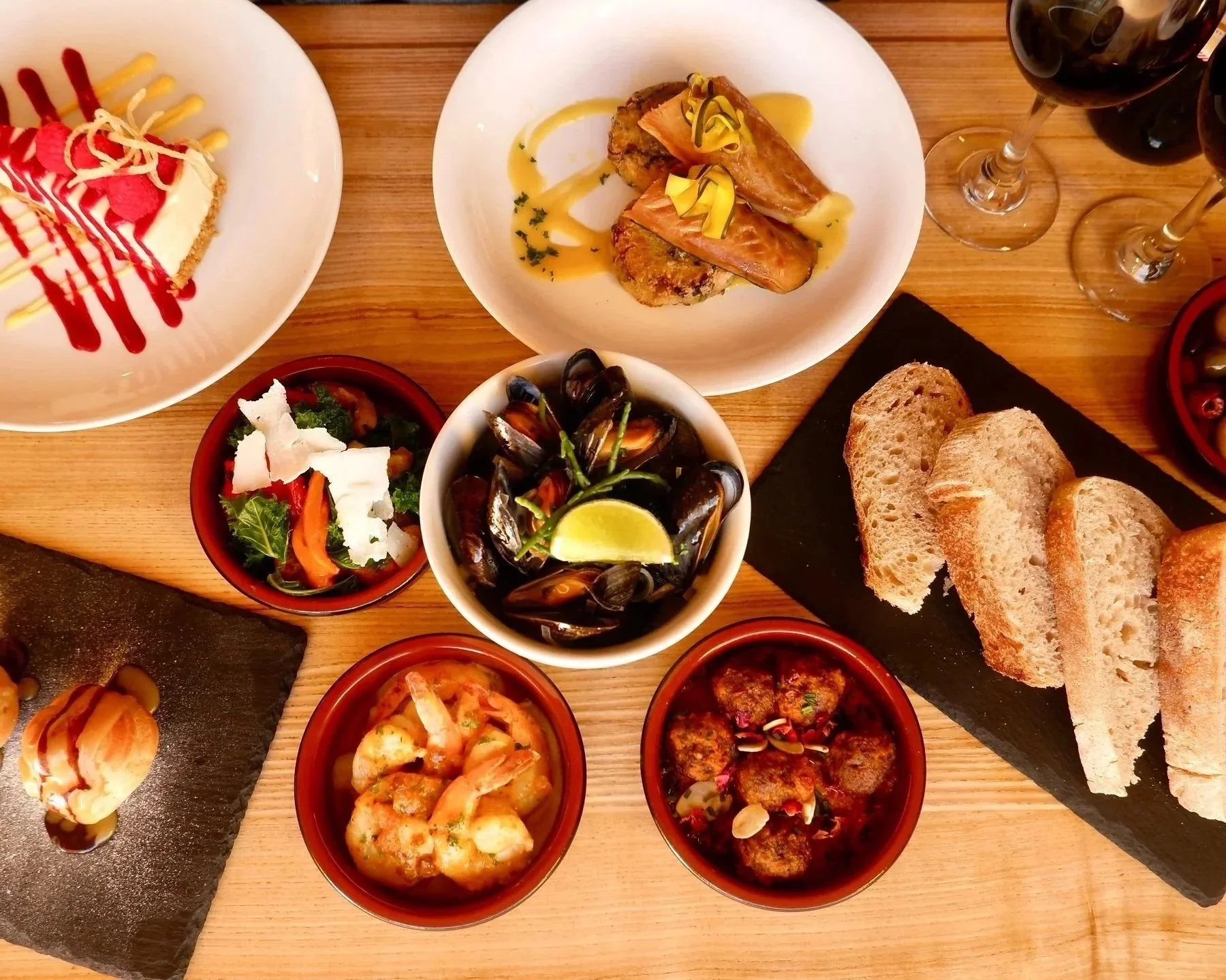 Assorted Mediterranean dishes with bread, seafood, salads, and charcuterie on a wooden table.
