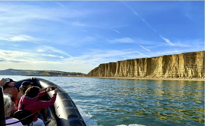 People on a boat looking at cliffs along a body of water under a blue sky with clouds.