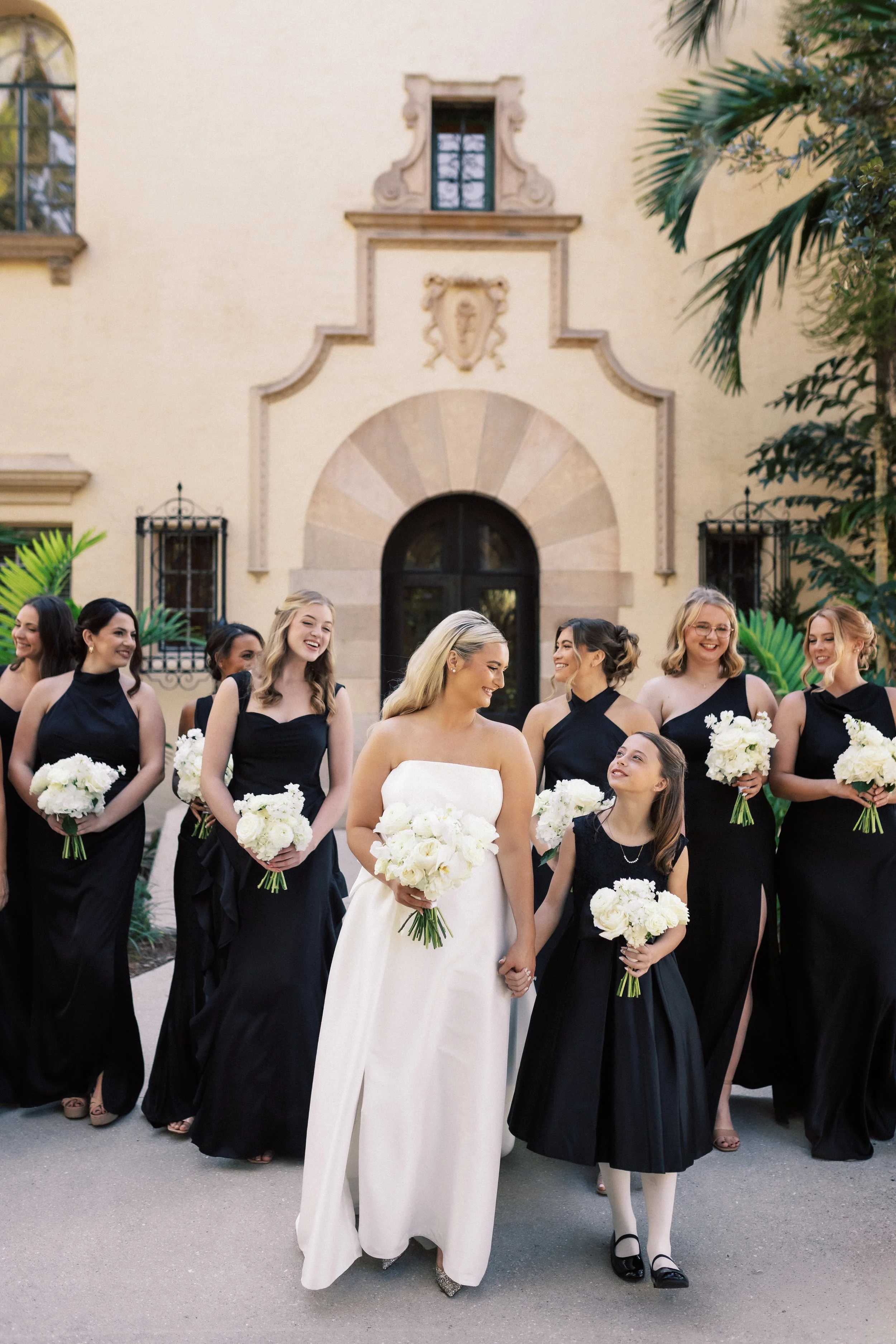 Bridal party of women with flowers, standing outdoors in front of a historic building, celebrating a wedding.