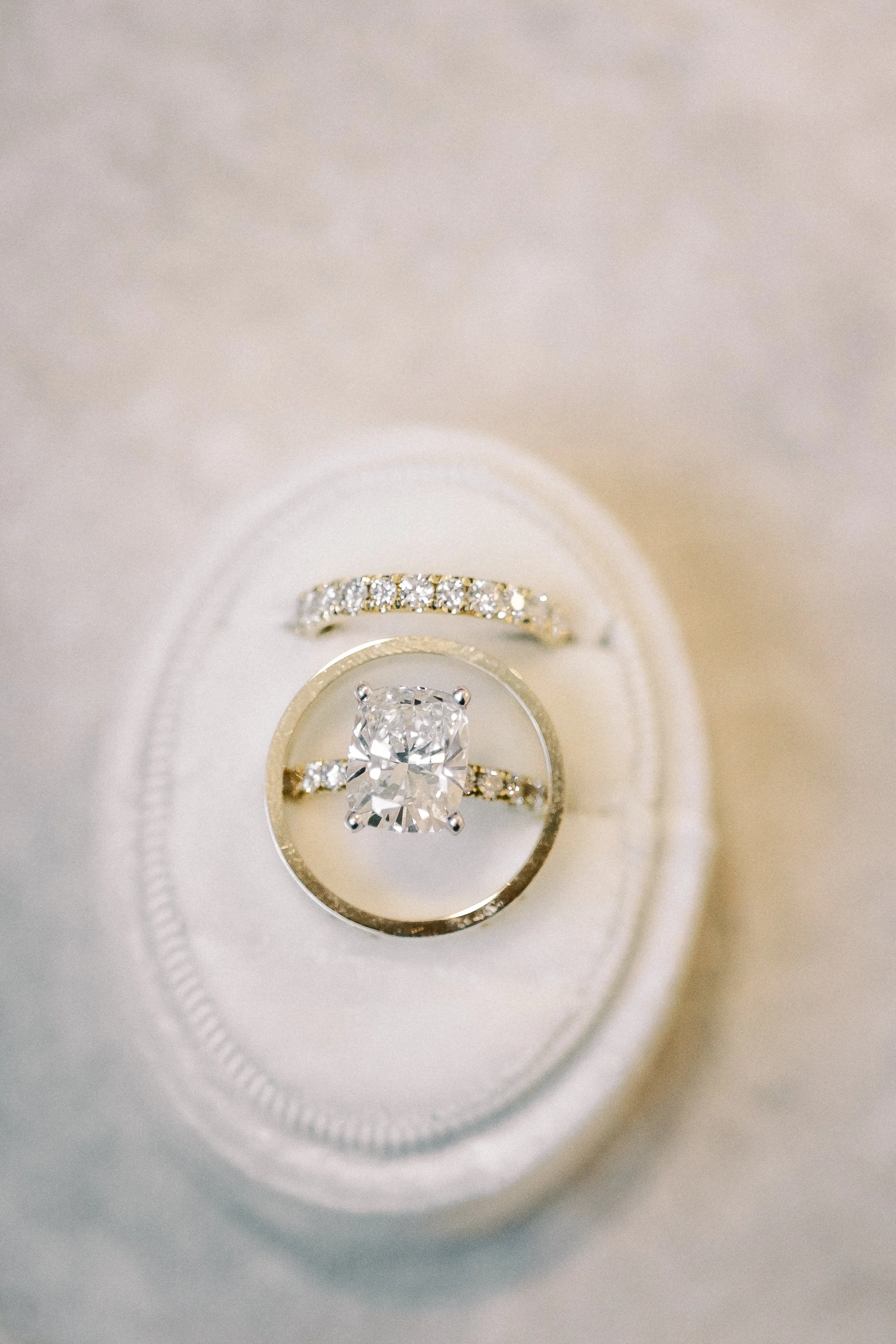 Close-up of a set of wedding rings, including an engagement ring with a large central diamond and a wedding band with smaller diamonds, placed on a white cushion.