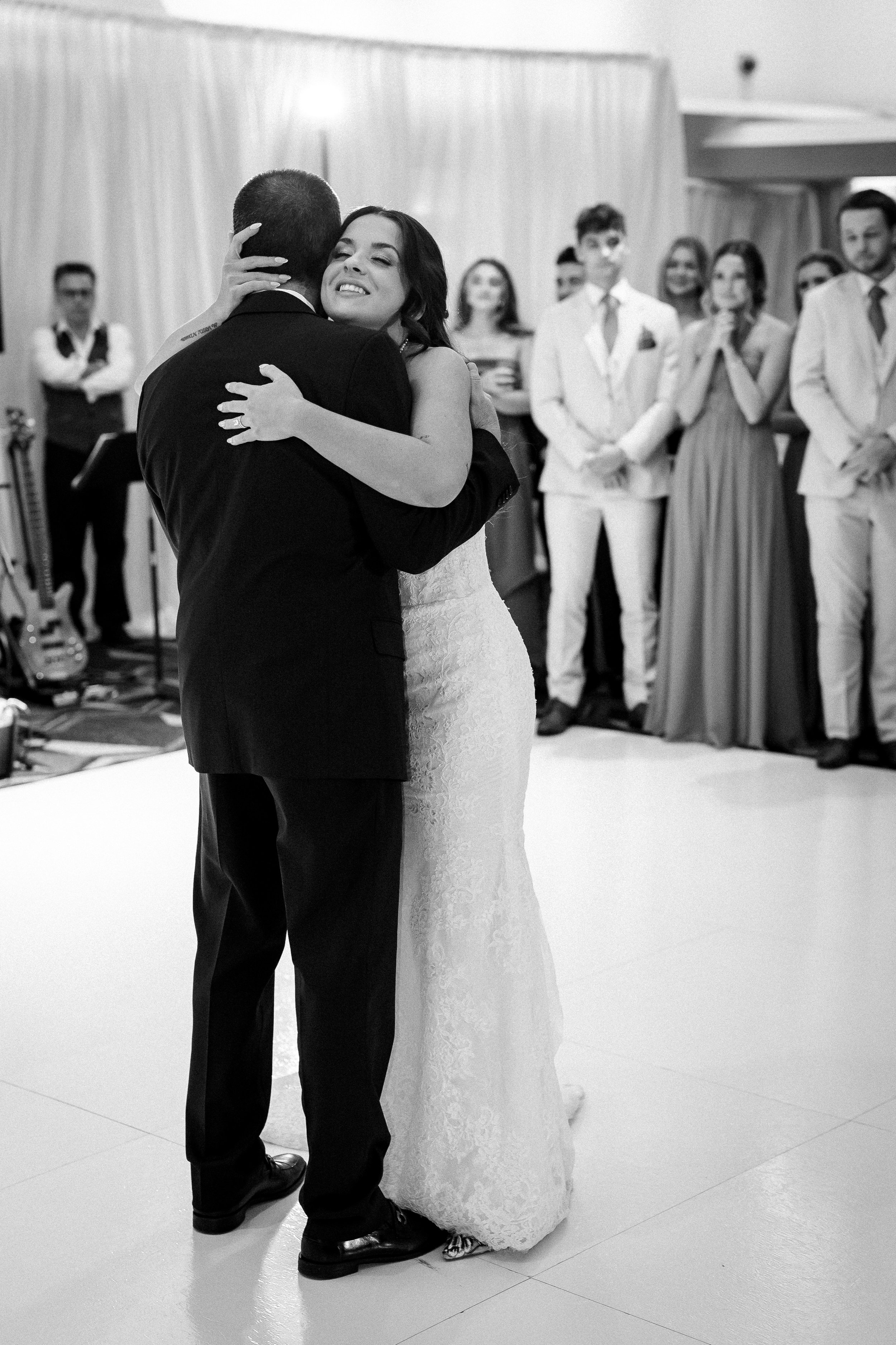 A bride and groom share their first dance at their wedding reception, surrounded by friends and family.