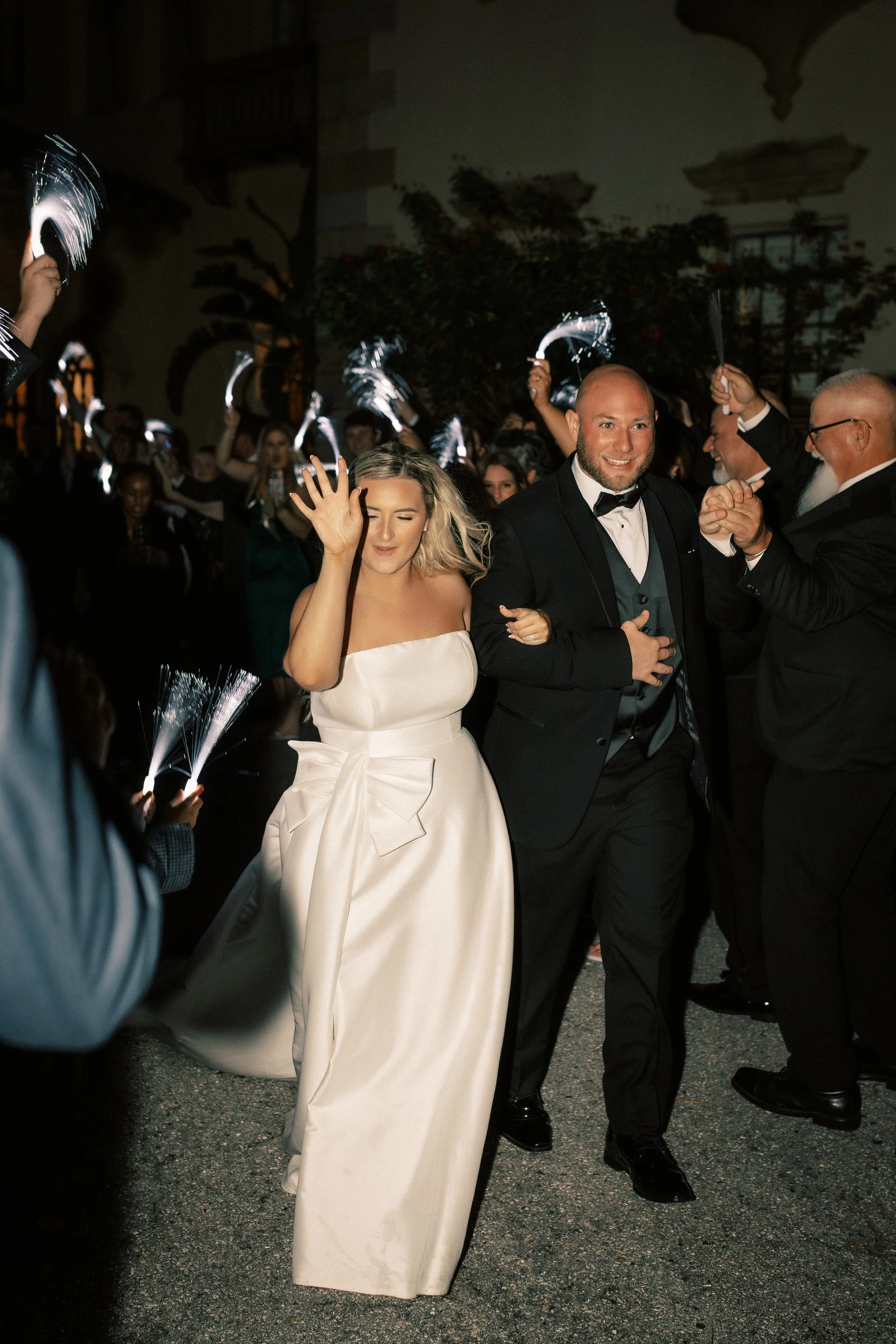 Couple in wedding attire dancing at nighttime with guests surrounding them, holding sparklers.