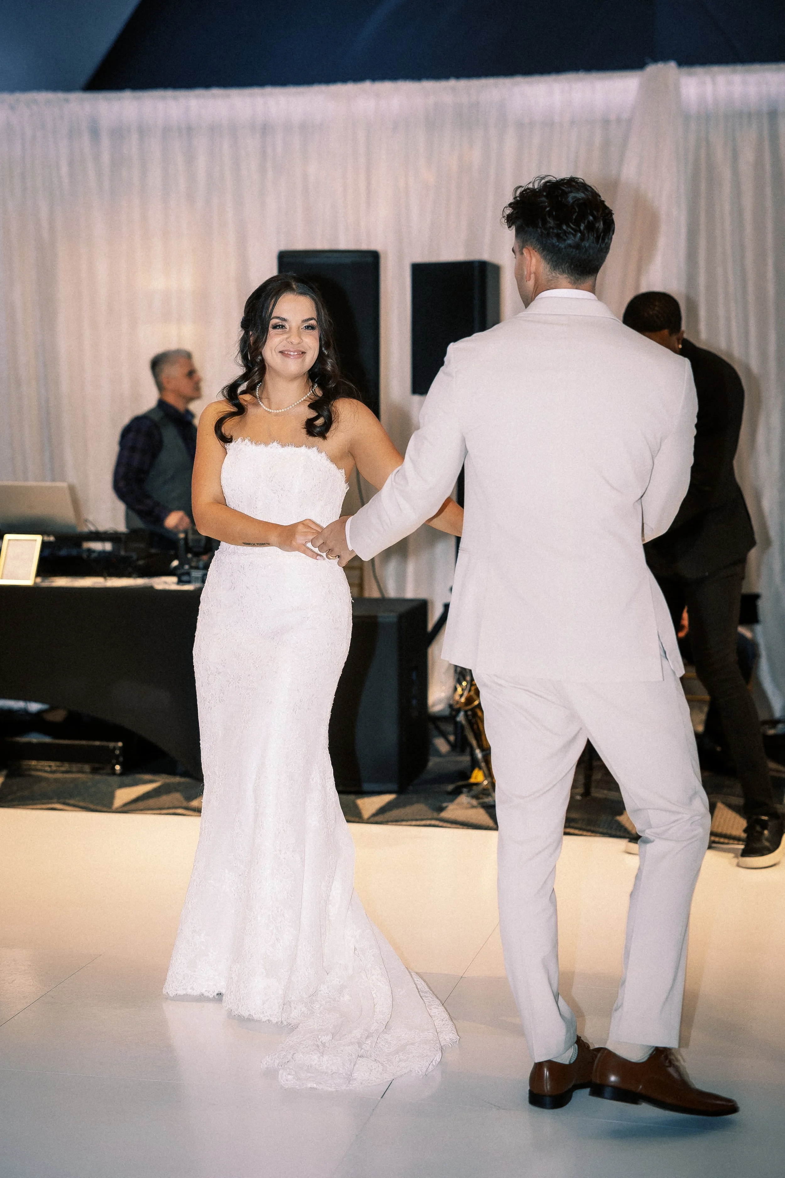 Bride in a white wedding dress dancing with groom in a white suit at wedding reception.