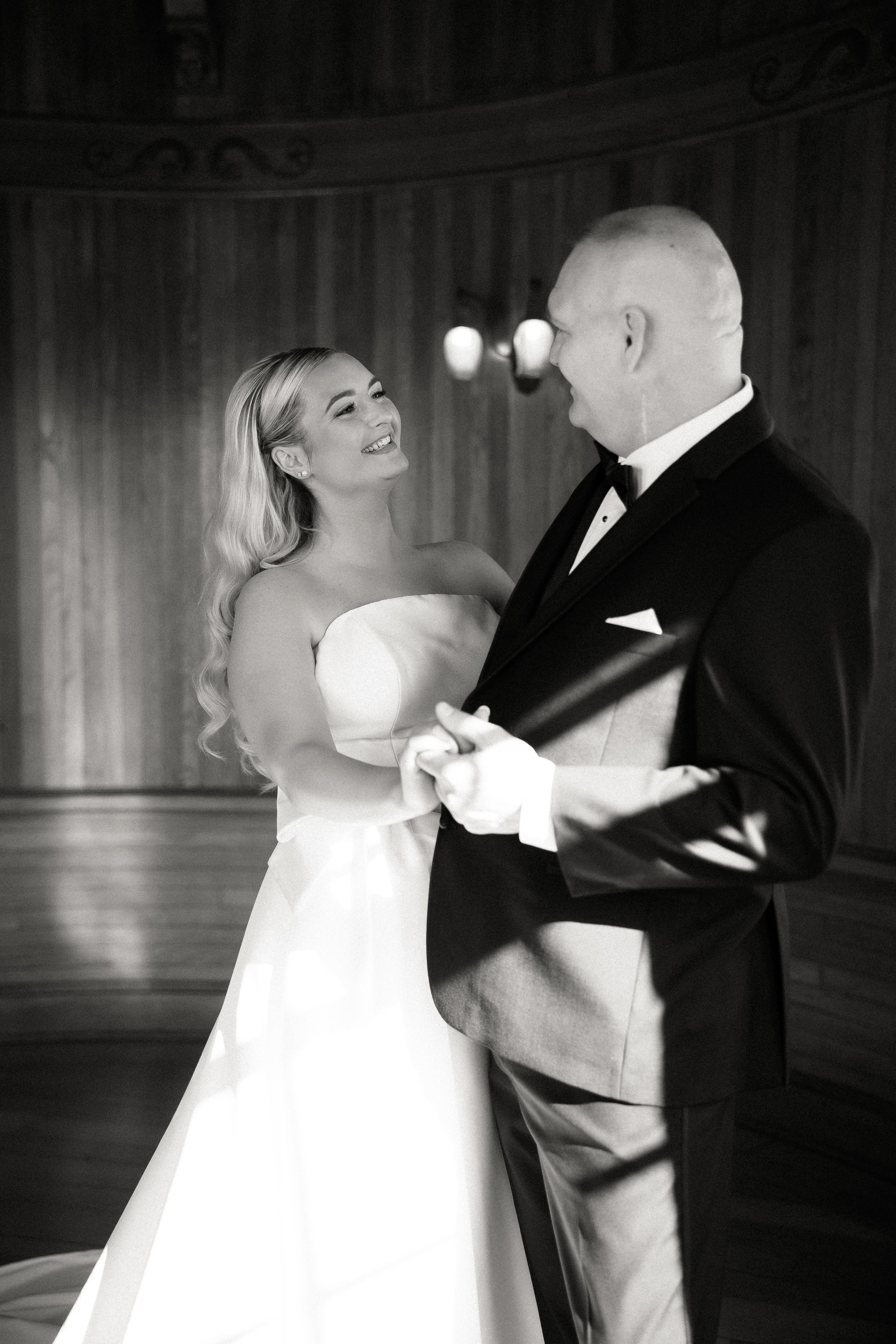 A bride with long hair smiling at her groom during their wedding ceremony in a wood-paneled room.
