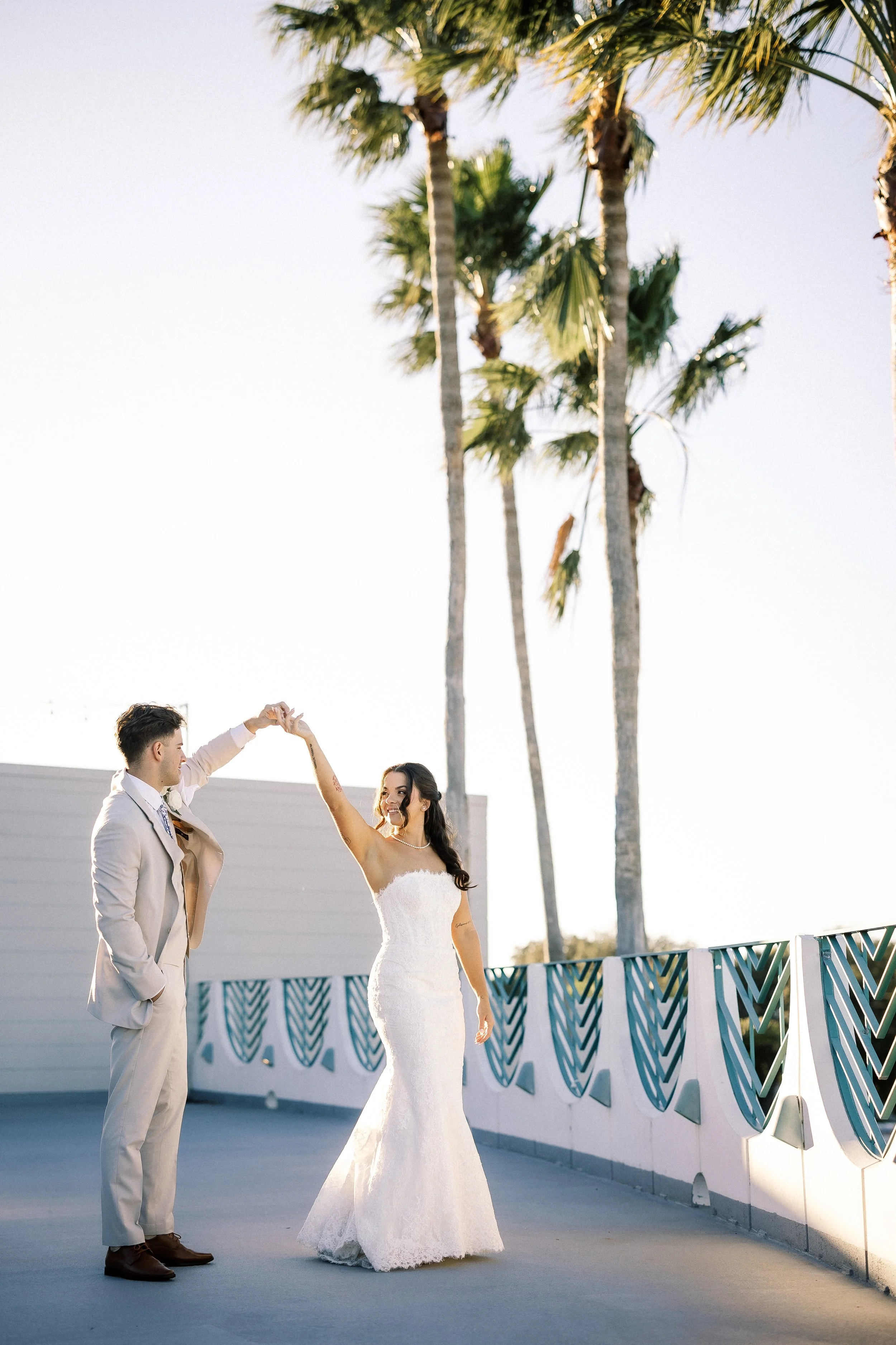 A bride and groom dance on a rooftop with palm trees in the background.