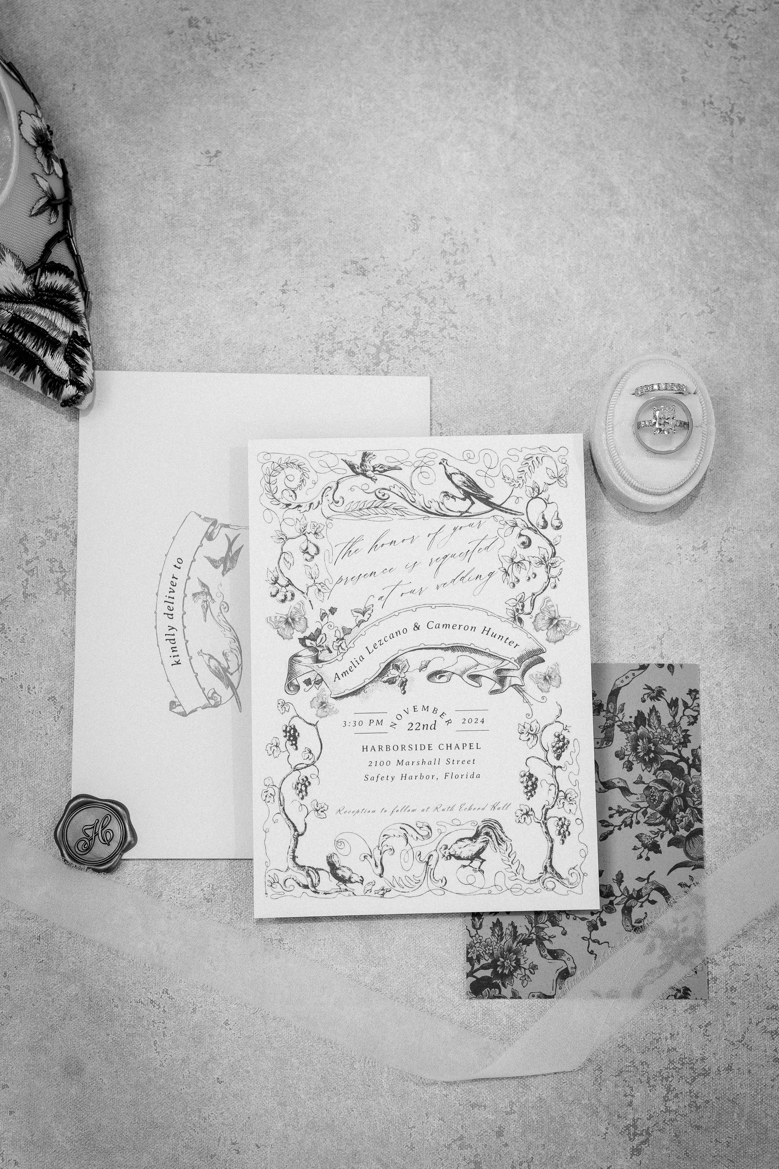 Wedding invitation with floral and bird illustrations, ring box, wax seal, and decorative paper, set on a table