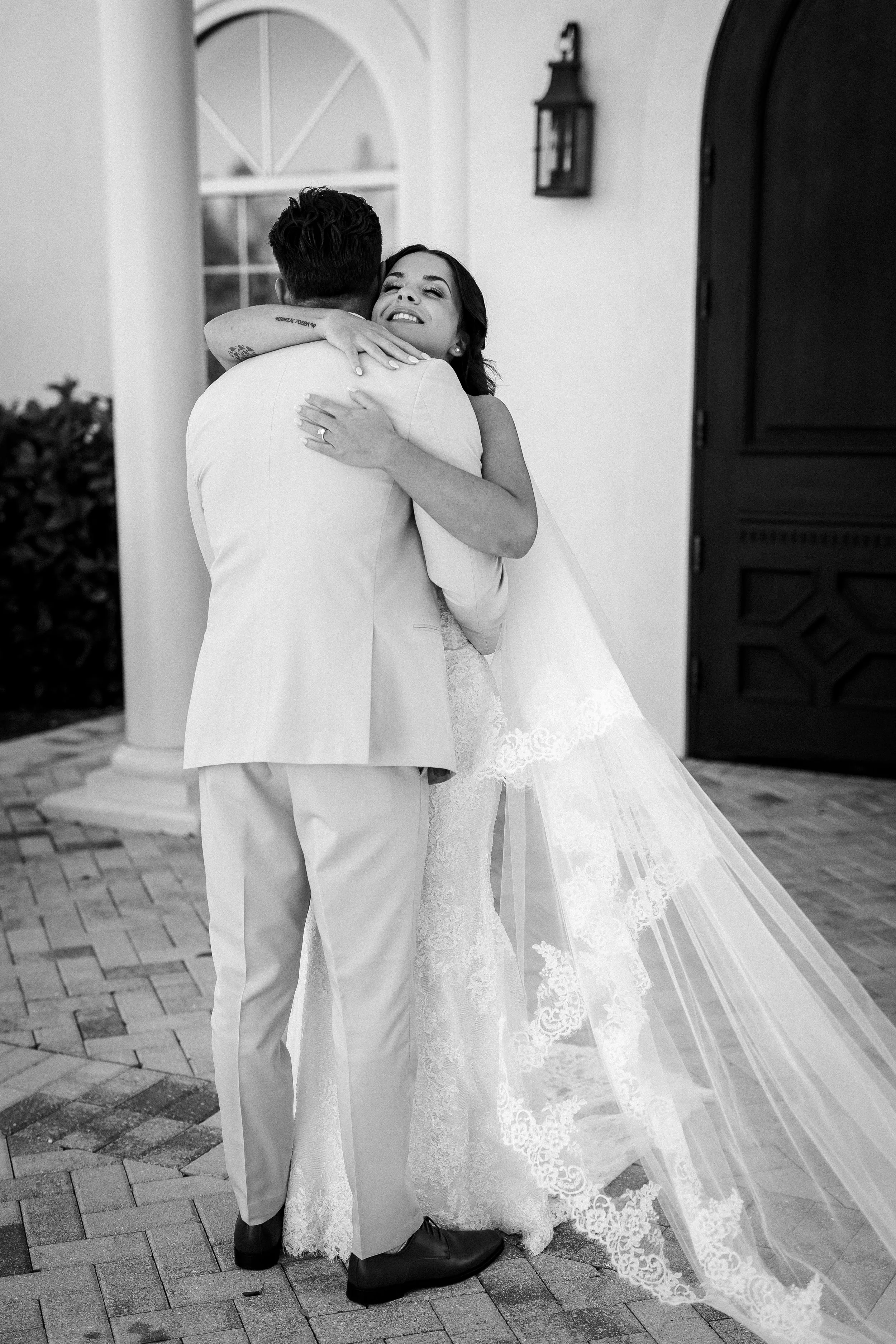 A bride and groom hugging outside a building at sunset, with the bride smiling.