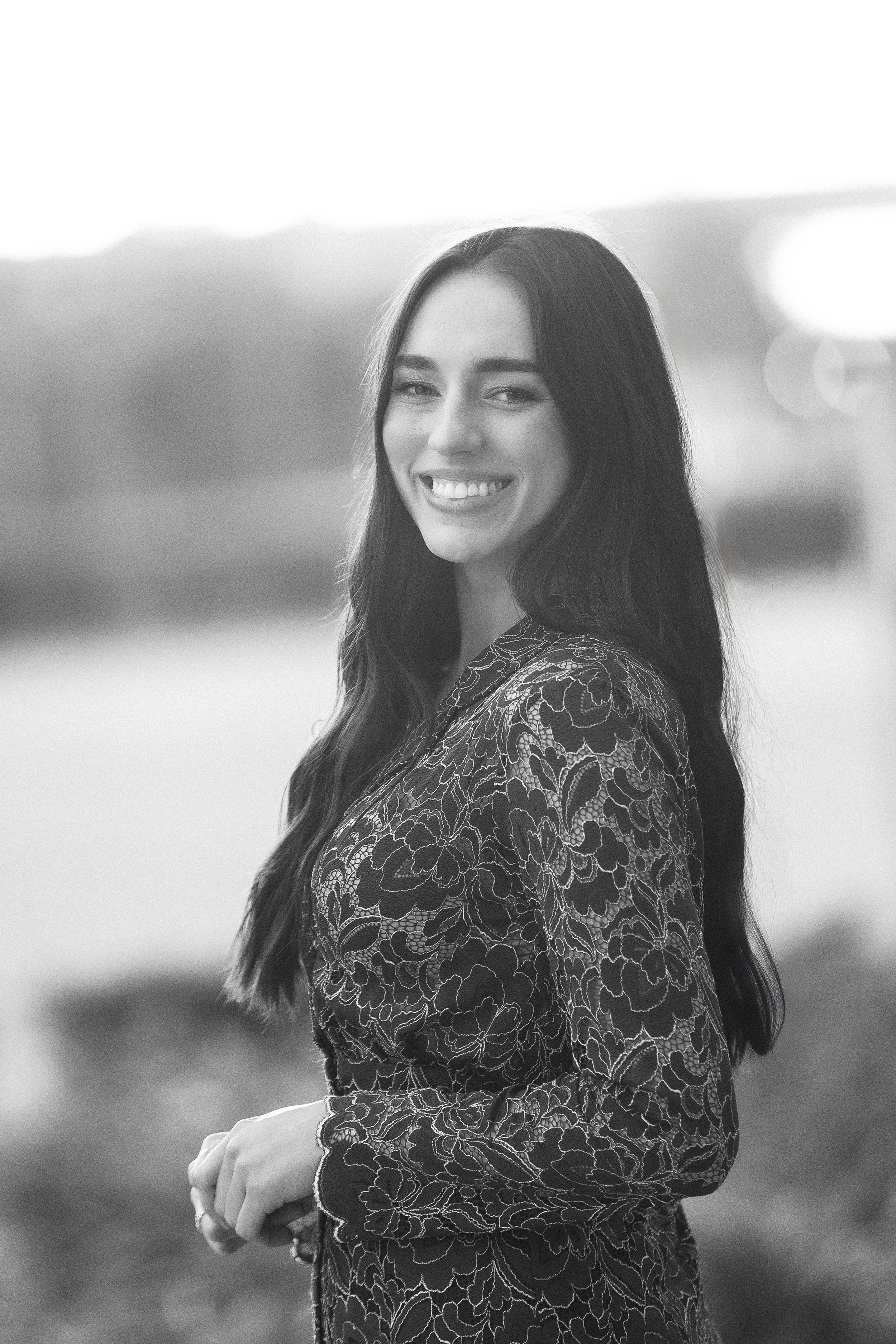 Amelia Island wedding photographer, Savannah Wedding Photographer, Black and white portrait of a smiling woman with long dark hair, wearing a floral patterned dress, standing outdoors.