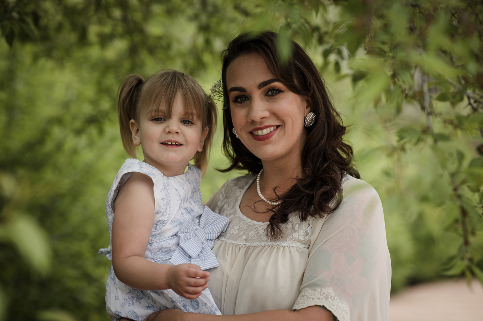 Family of five with a dog enjoying a sunny day outdoors in a park with green trees.
