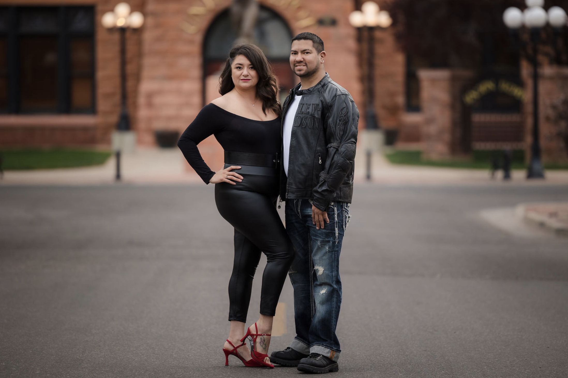 A young man with tousled blond hair and a serious expression, wearing a light gray T-shirt with buttons, standing outdoors in front of a calm body of water and a blurred green landscape.