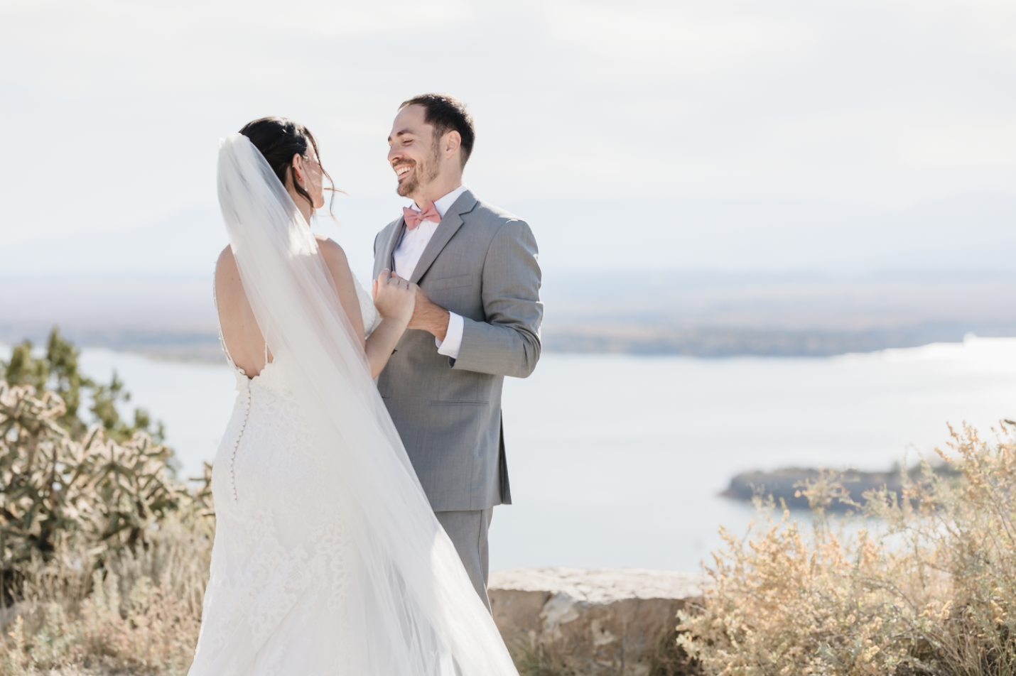 A young woman with curly brown hair, wearing a white dress, sitting on a fallen tree trunk in a lush green forest, smiling at the camera.