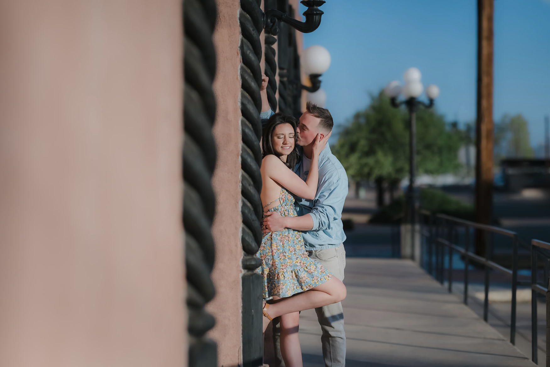 A pregnant woman in a yellow dress standing outdoors in a park at sunset, smiling and holding her belly, with trees and grass in the background.
