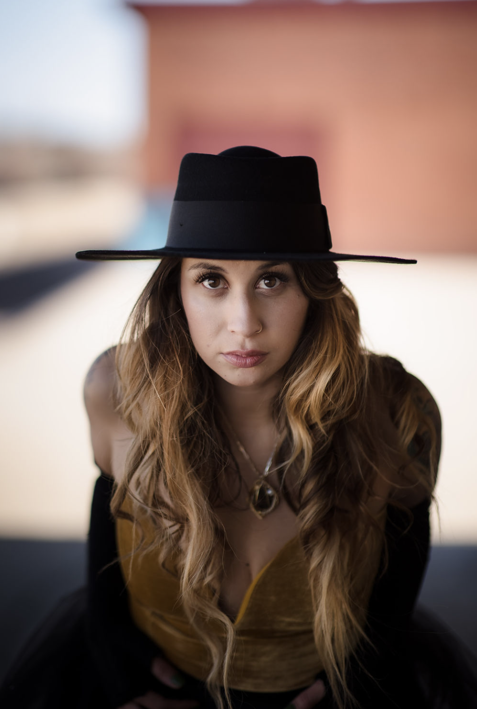 A young girl in a yellow dress with ruffled sleeves and black buttons sitting on a person's shoulder outdoors, smiling and looking at someone out of frame, with trees and greenery in the background.