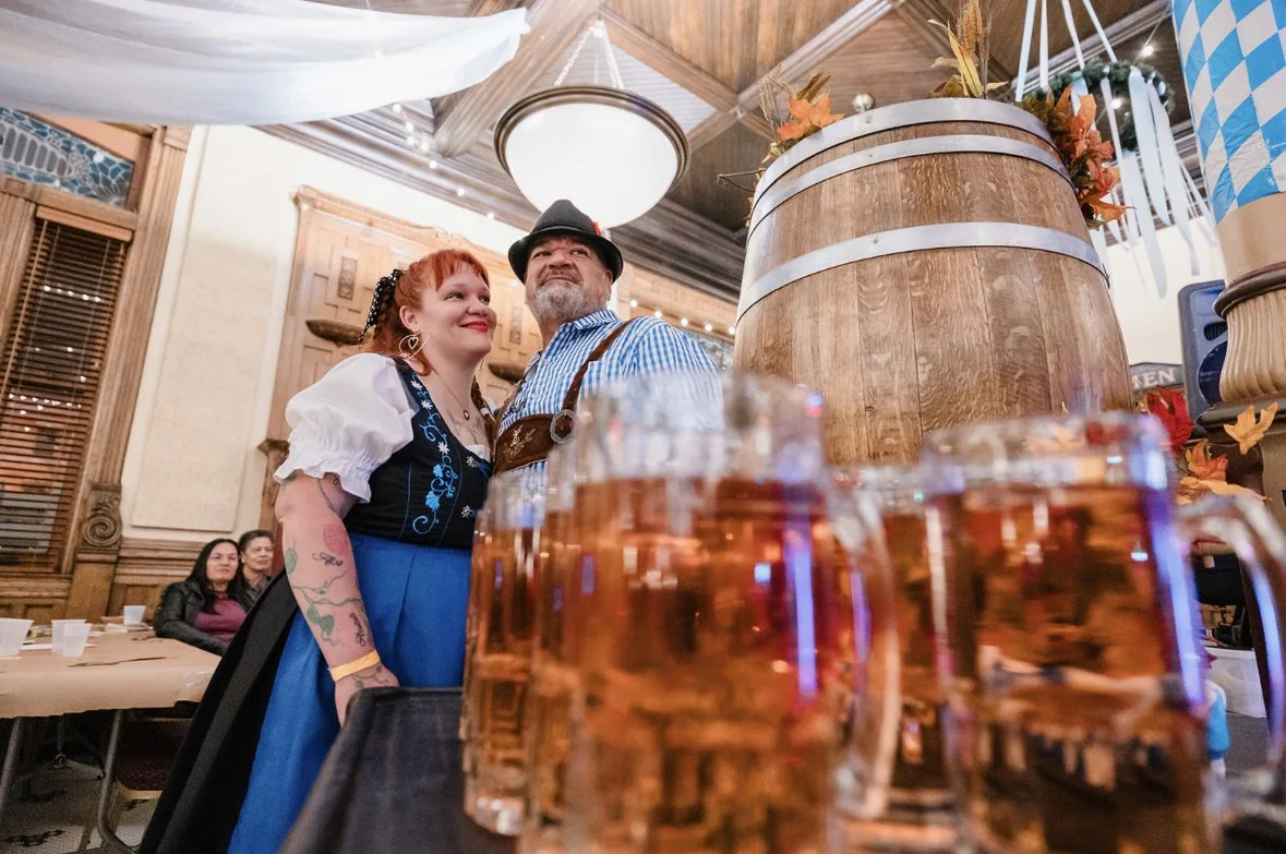 A young girl in a yellow dress with ruffled sleeves and black buttons sitting on a person's shoulder outdoors, smiling and looking at someone out of frame, with trees and greenery in the background.