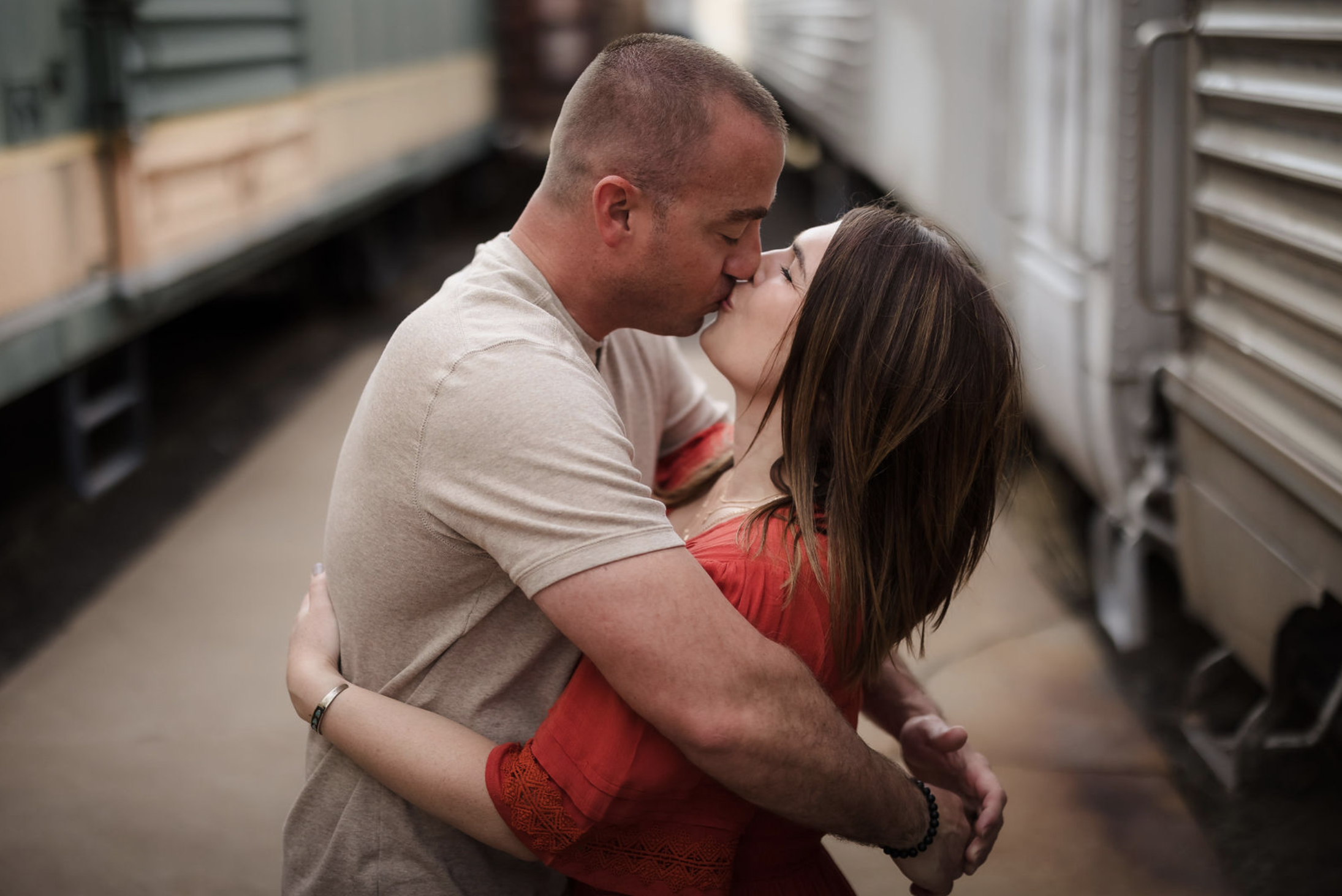 A pregnant woman in a yellow dress standing outdoors in a park at sunset, smiling and holding her belly, with trees and grass in the background.