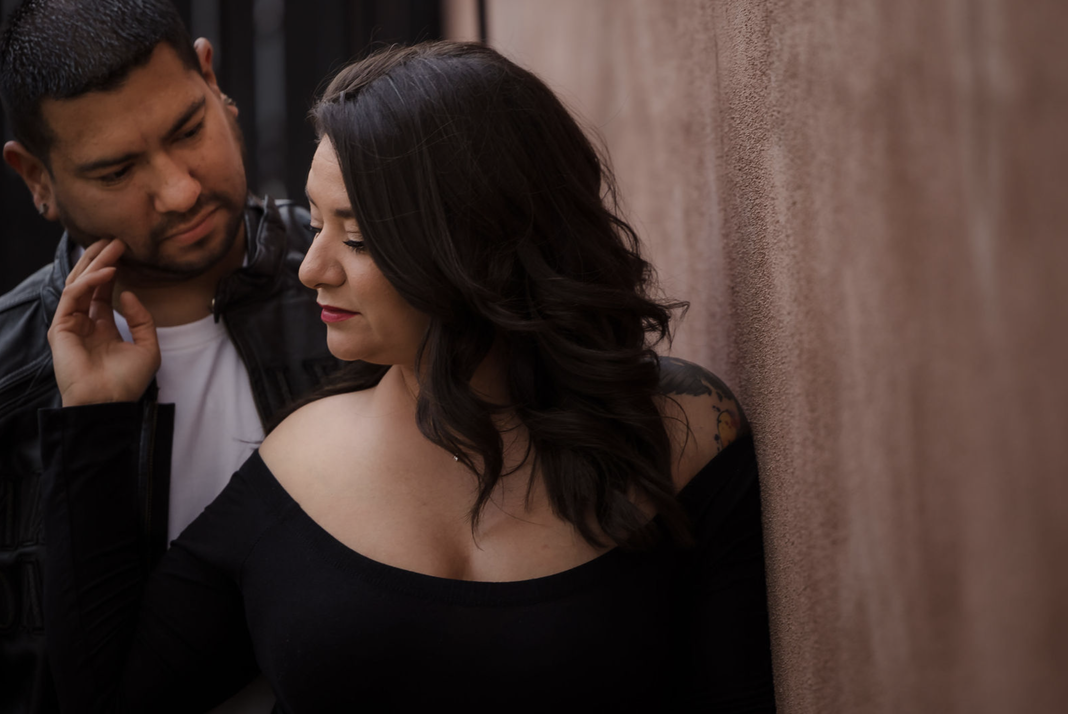 A young woman with curly brown hair, wearing a white dress, sitting on a fallen tree trunk in a lush green forest, smiling at the camera.