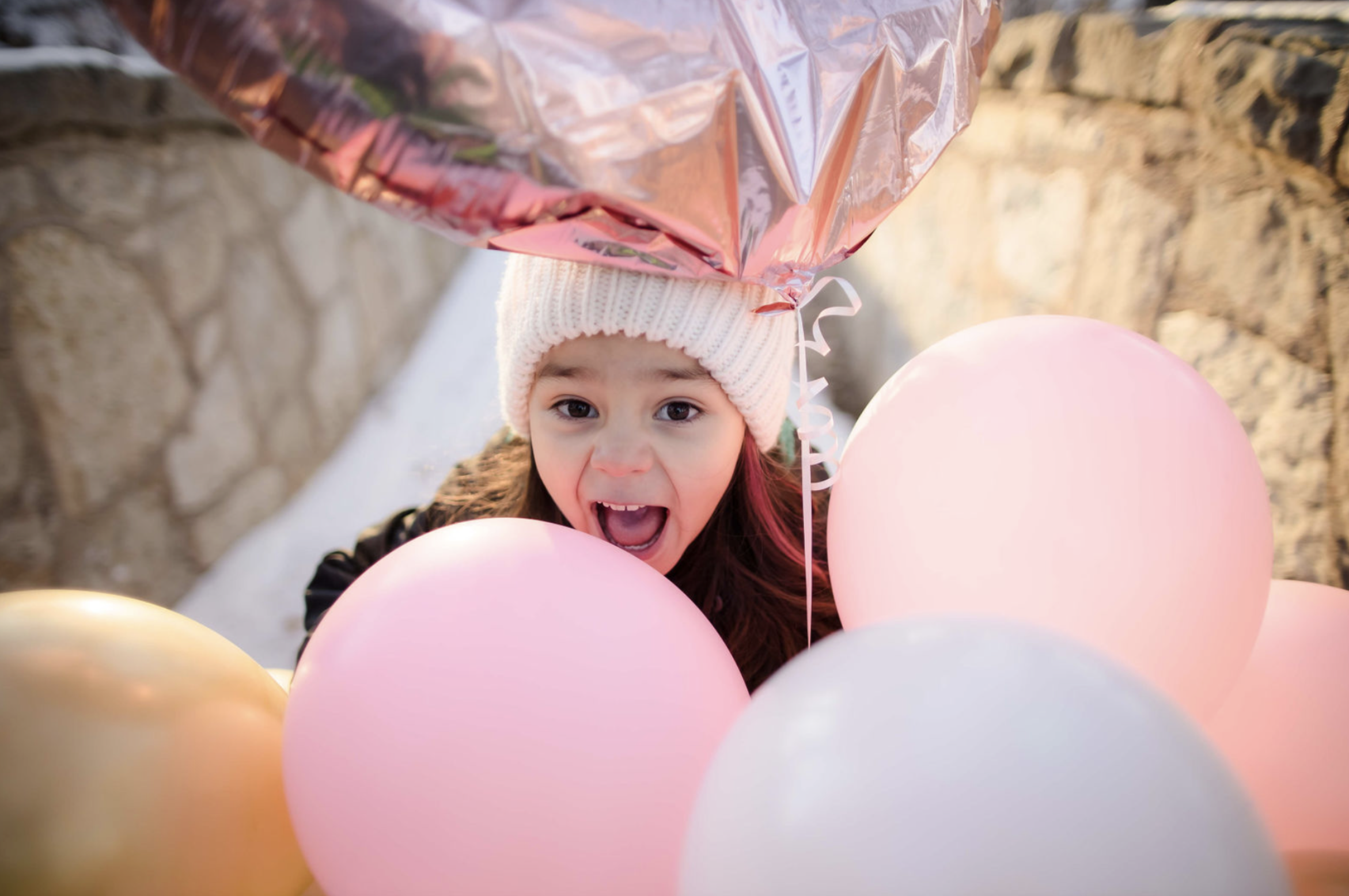A young woman with curly brown hair, wearing a white dress, sitting on a fallen tree trunk in a lush green forest, smiling at the camera.