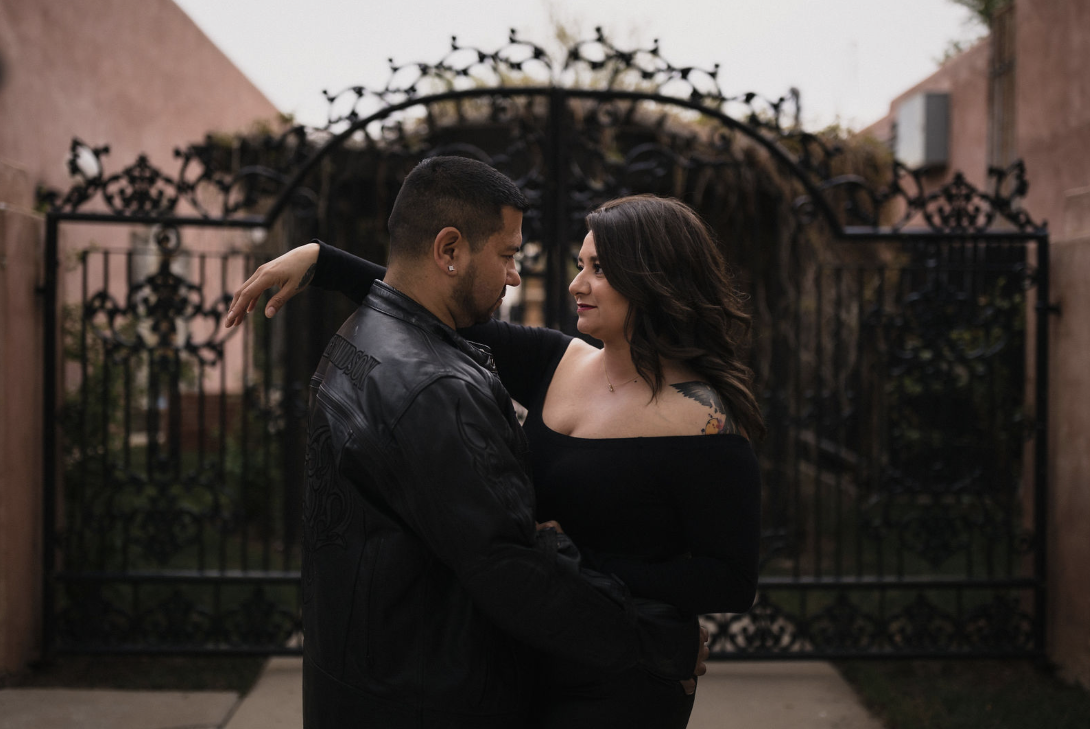 A young man with tousled blond hair and a serious expression, wearing a light gray T-shirt with buttons, standing outdoors in front of a calm body of water and a blurred green landscape.