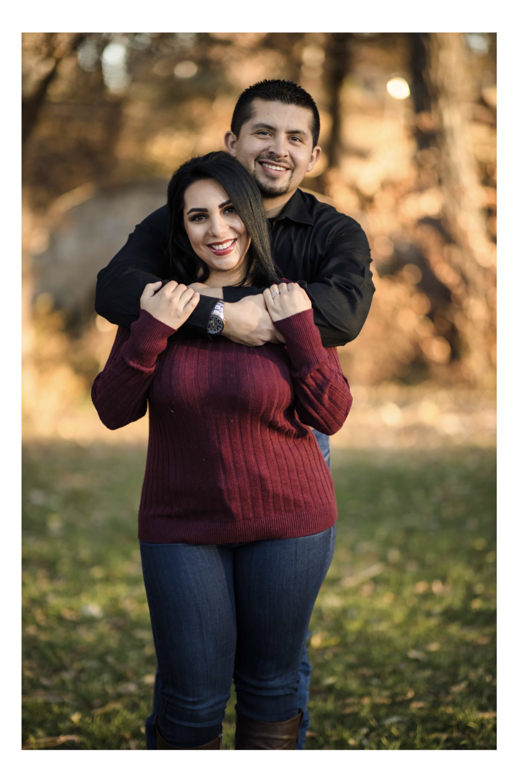 Black and white photo of a man and woman standing outdoors among trees, facing opposite directions with serious expressions, the woman in the foreground and the man slightly behind.