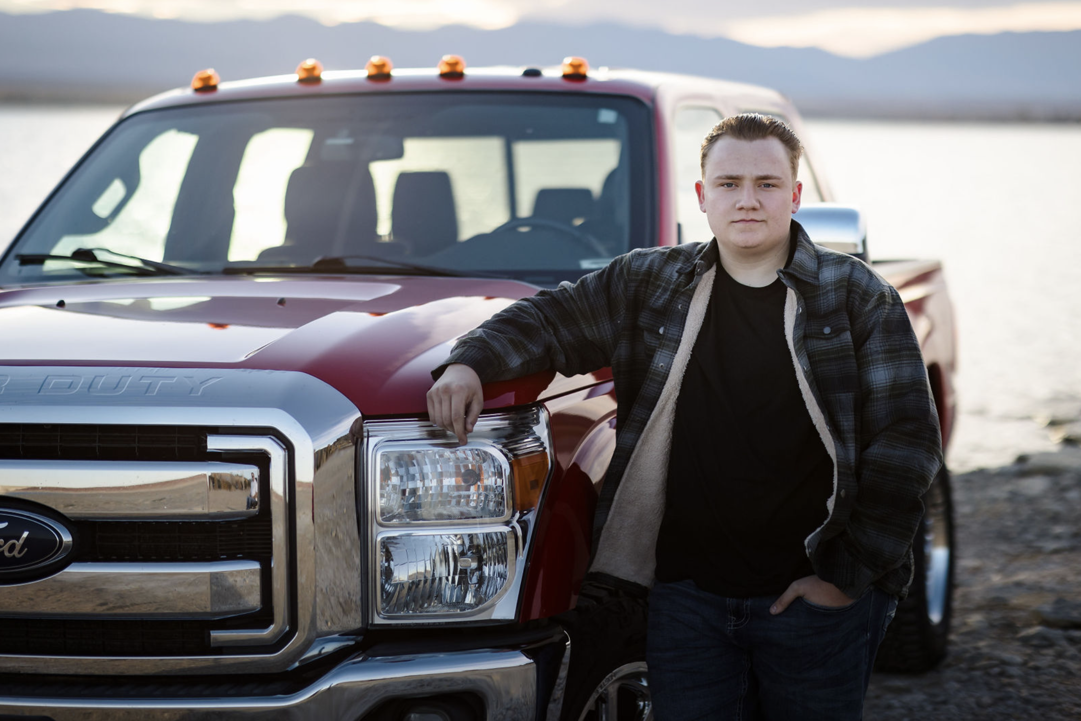 A young girl in a yellow dress with ruffled sleeves and black buttons sitting on a person's shoulder outdoors, smiling and looking at someone out of frame, with trees and greenery in the background.