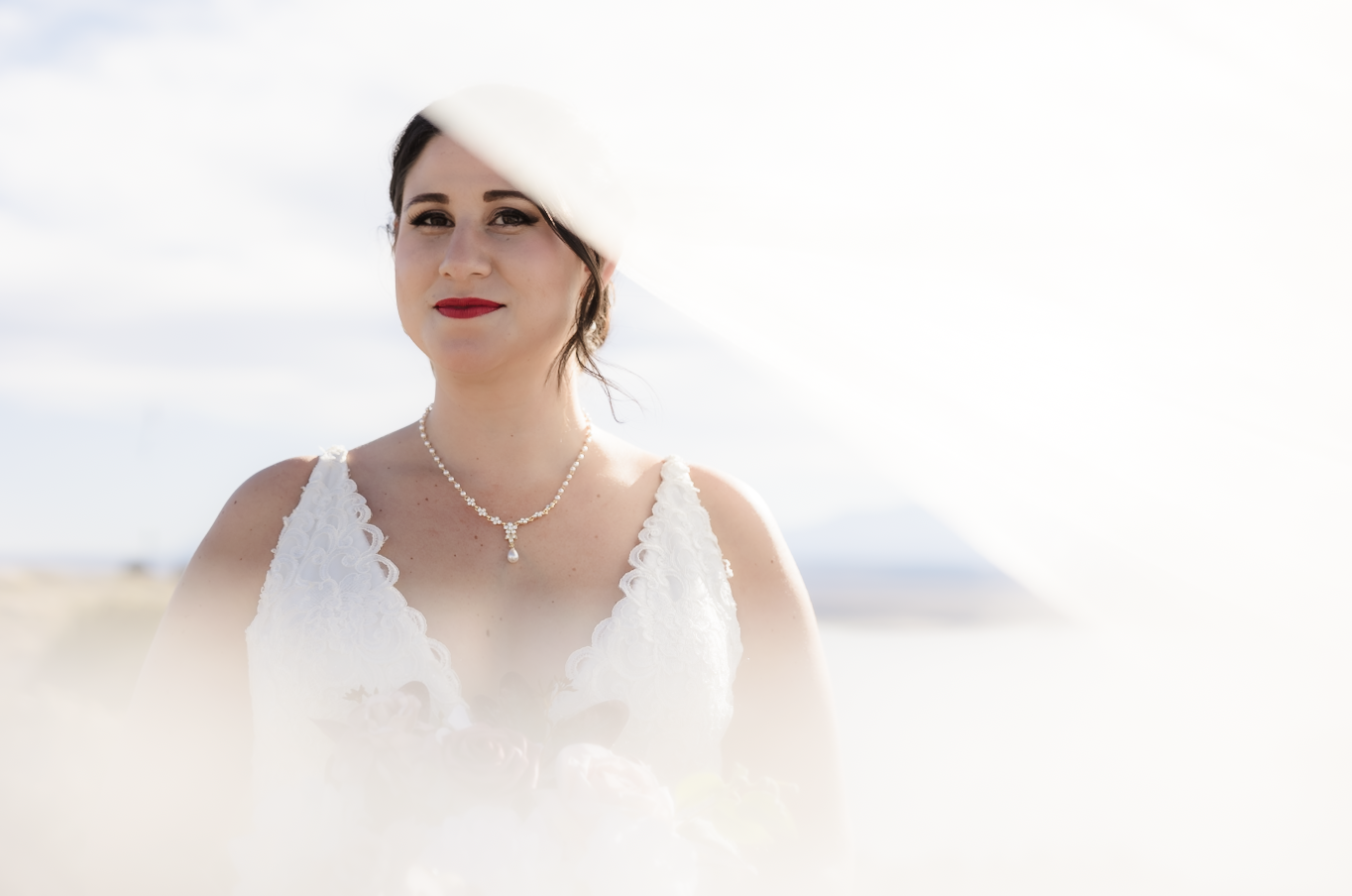 A woman and a young girl are smiling and hugging outdoors near a body of water during autumn, with colorful fall trees in the background.