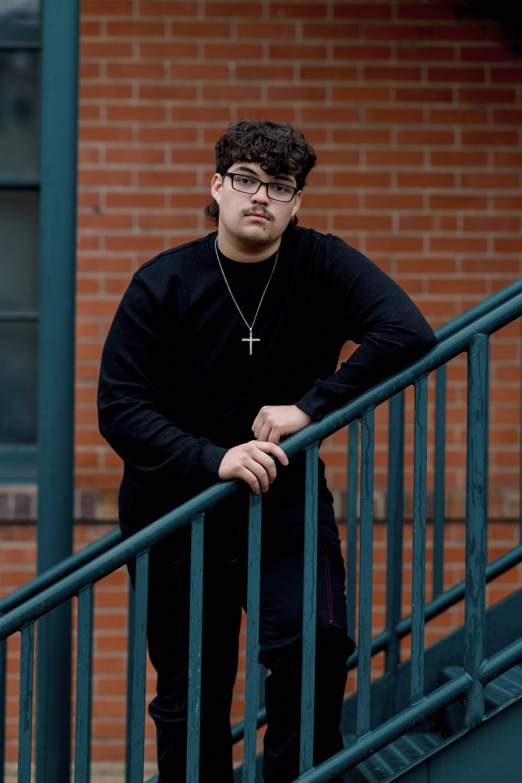 Black and white photo of a man and woman standing outdoors among trees, facing opposite directions with serious expressions, the woman in the foreground and the man slightly behind.