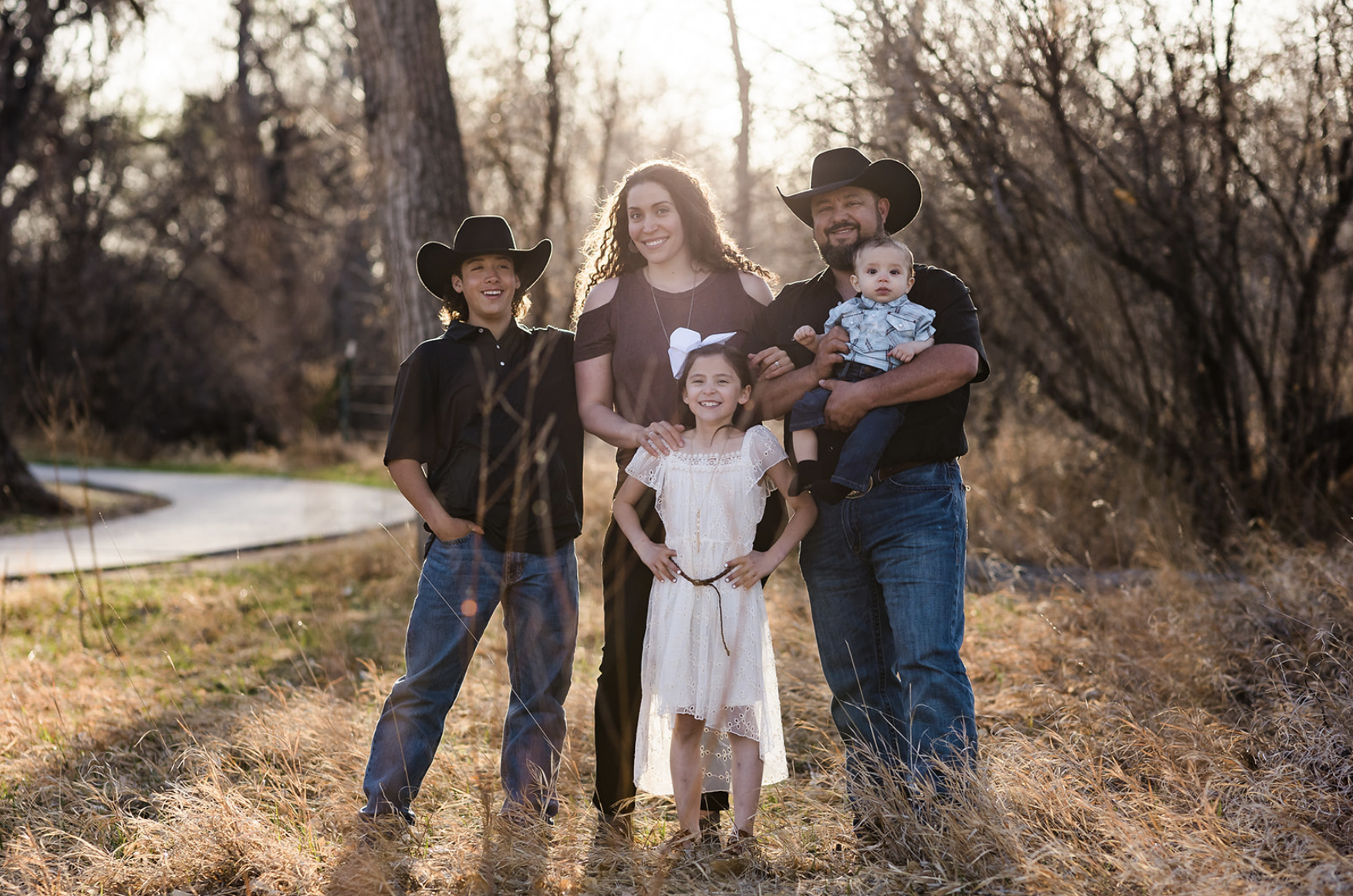 Family of five with a dog enjoying a sunny day outdoors in a park with green trees.