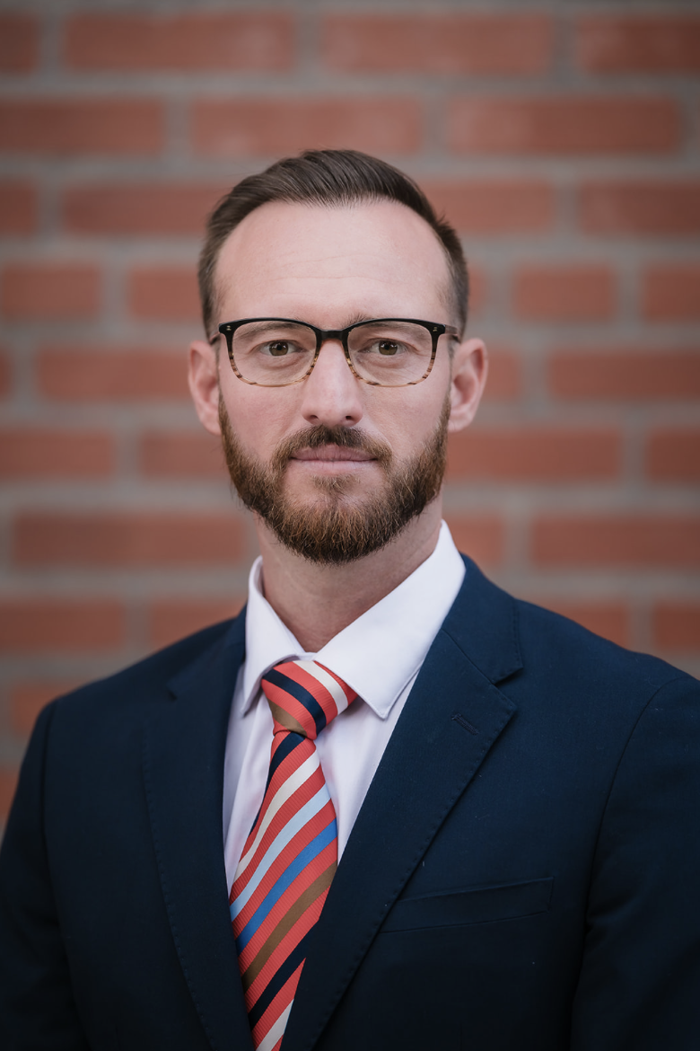 A woman in a black lace dress standing in a field of tall grasses with a lake and forested hills in the background.