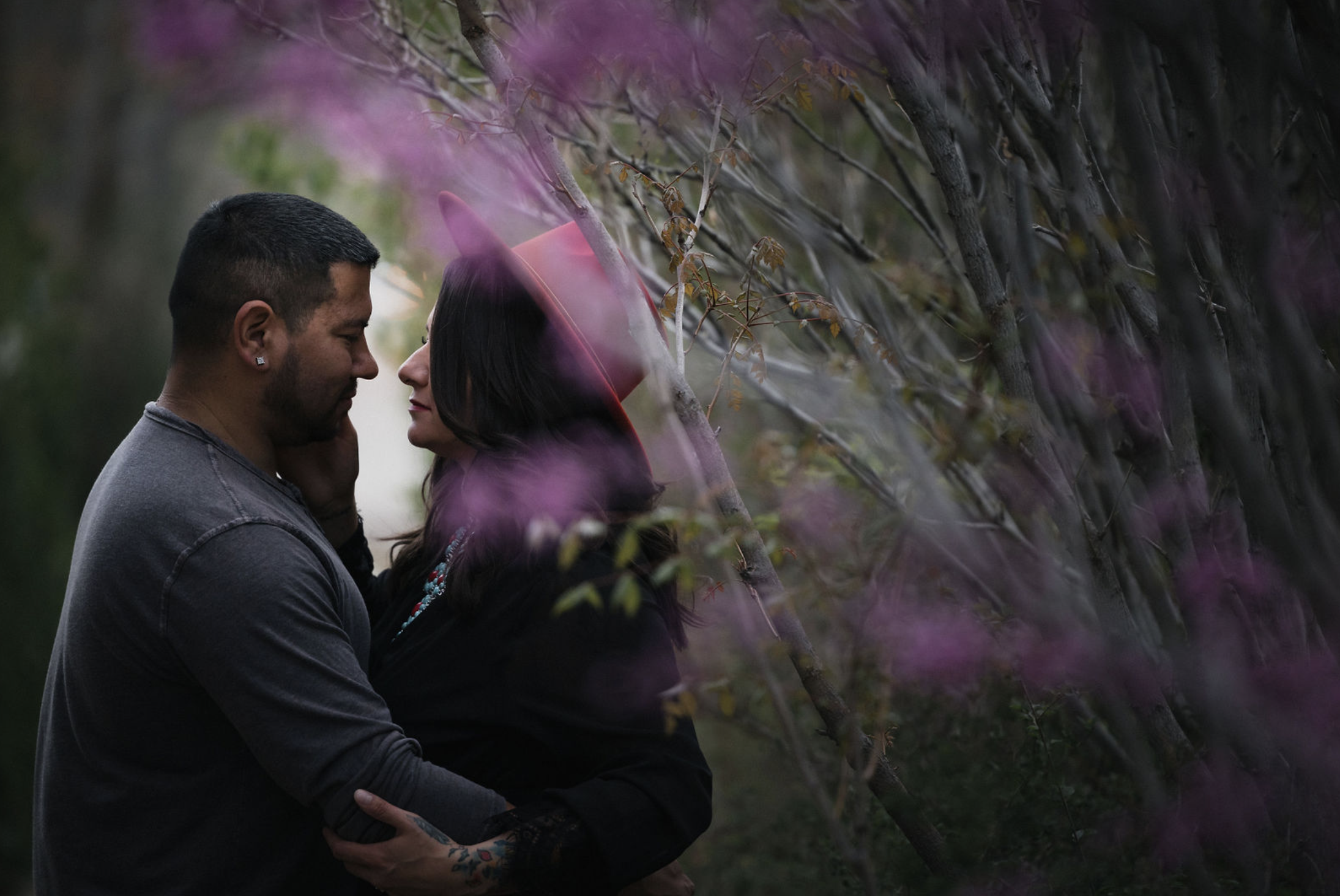 A young woman with curly brown hair, wearing a white dress, sitting on a fallen tree trunk in a lush green forest, smiling at the camera.