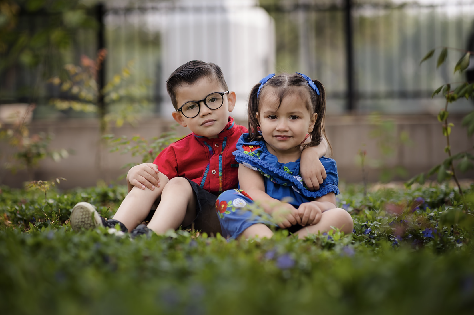 A woman and a young girl are smiling and hugging outdoors near a body of water during autumn, with colorful fall trees in the background.