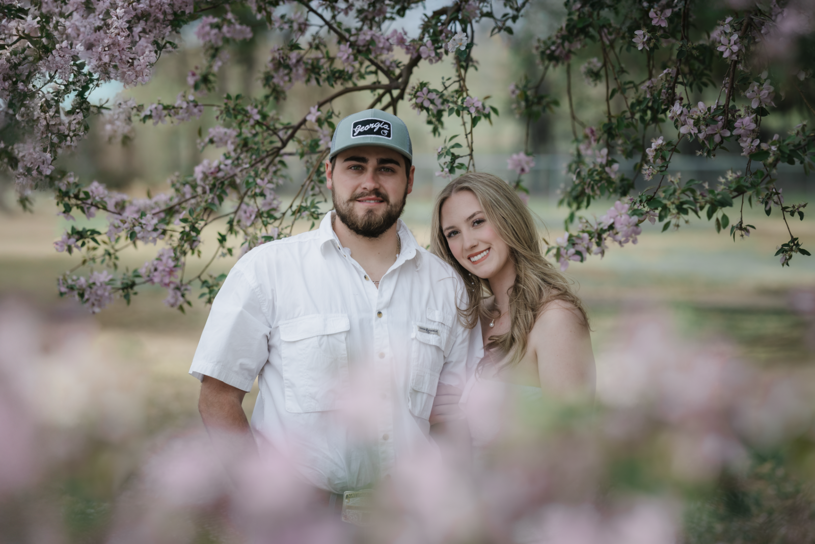 Two children playing near the edge of a lake during sunset, with trees in the background and the sun reflecting on the water.