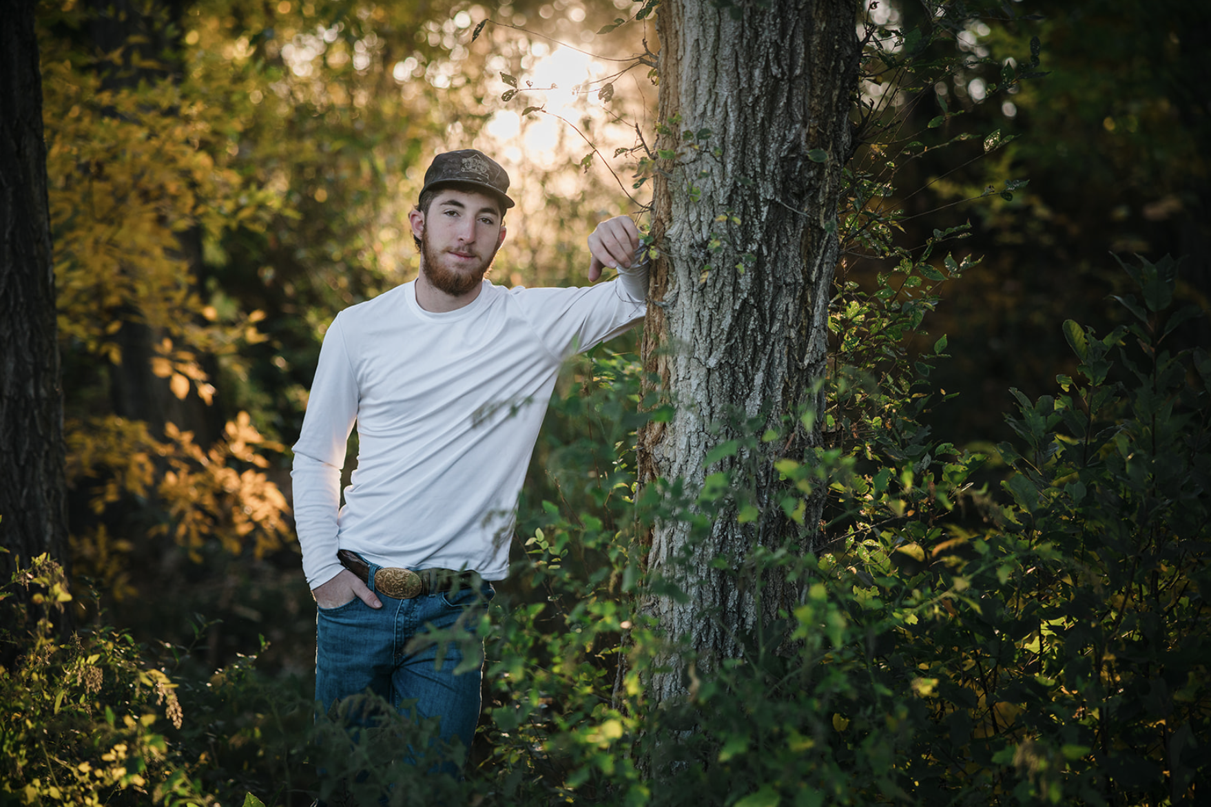 A young girl in a yellow dress with ruffled sleeves and black buttons sitting on a person's shoulder outdoors, smiling and looking at someone out of frame, with trees and greenery in the background.