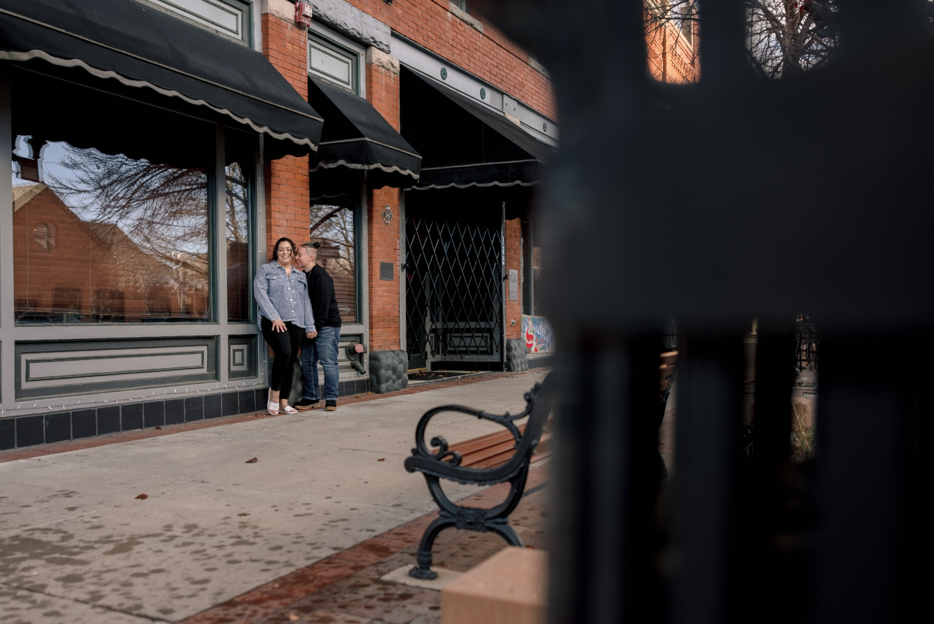 A young girl and boy hugging on a dirt path in a wooded area with autumn leaves, with a man and woman standing in the background, slightly out of focus.