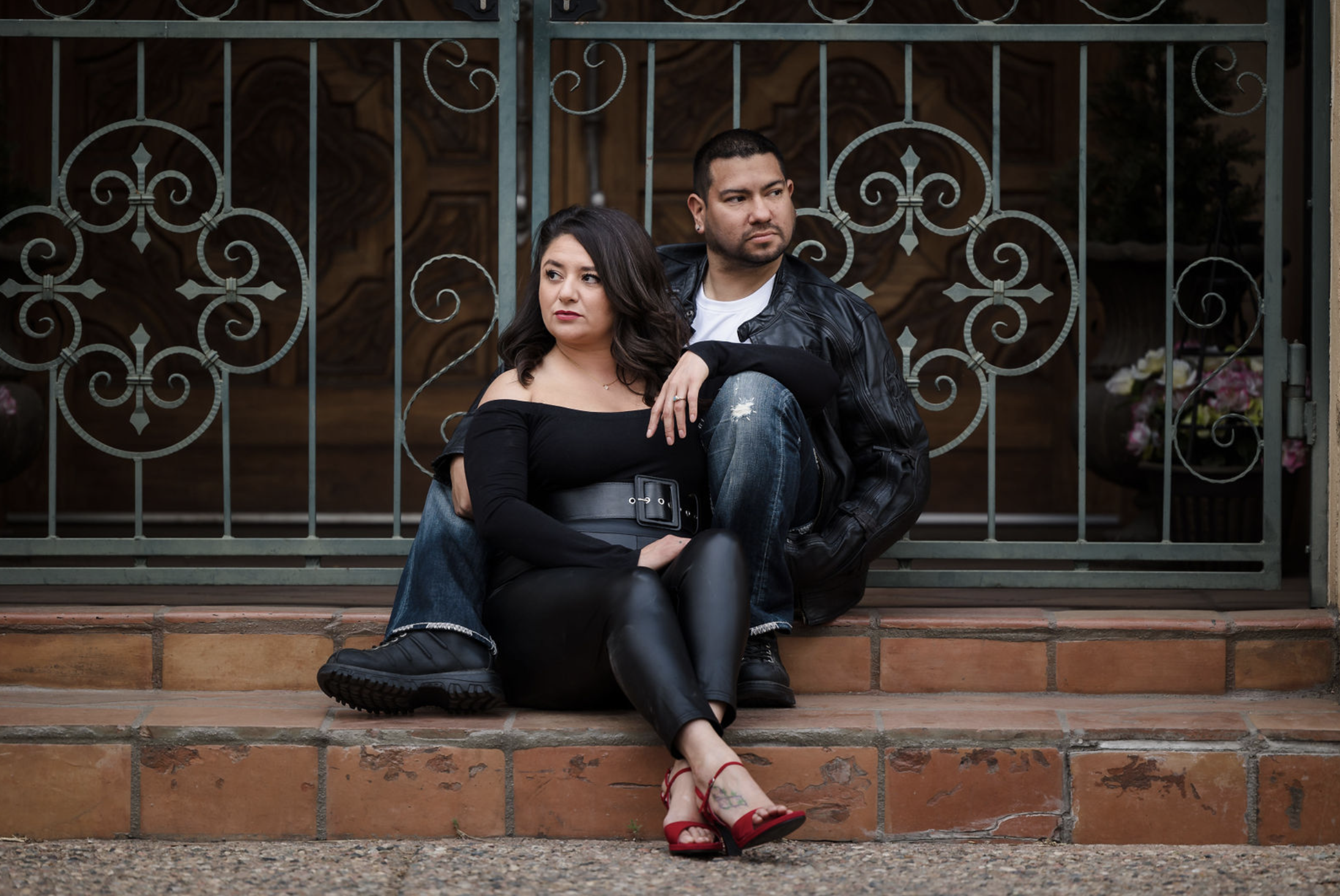 Young man sitting outdoors on grass near a tree, wearing a colorful floral shirt and blue jeans, with a thoughtful expression.