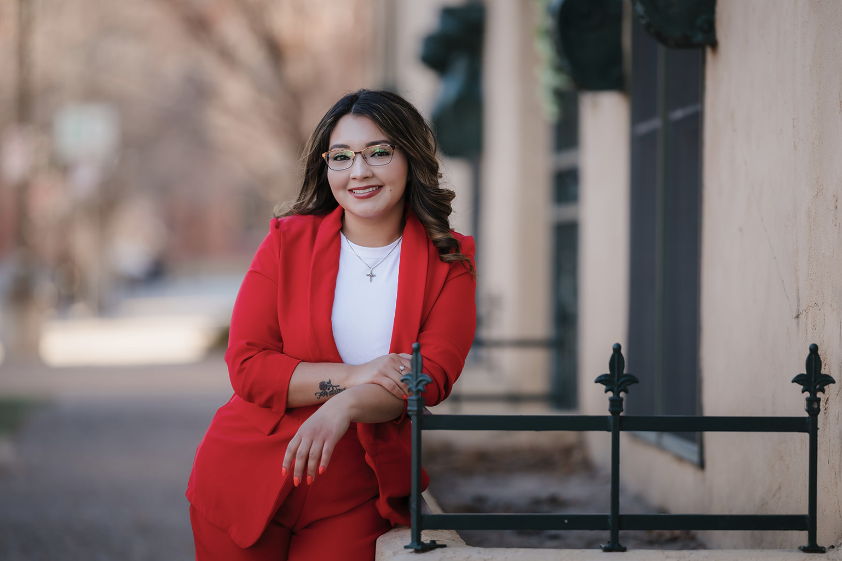 Woman in a navy blue dress walking through a grassy field with tall trees with yellow leaves in the background.