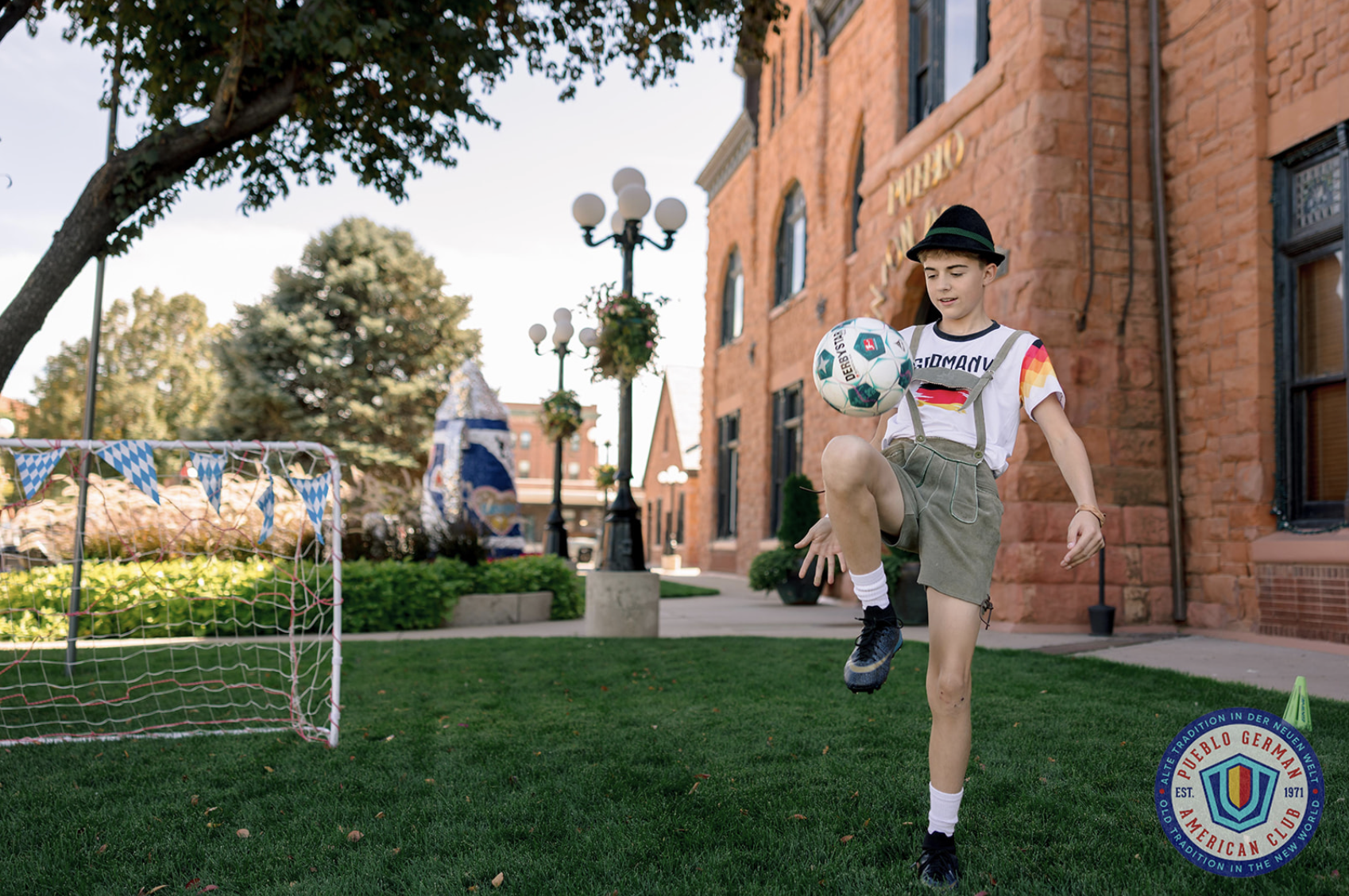 A pregnant woman in a yellow dress standing outdoors in a park at sunset, smiling and holding her belly, with trees and grass in the background.