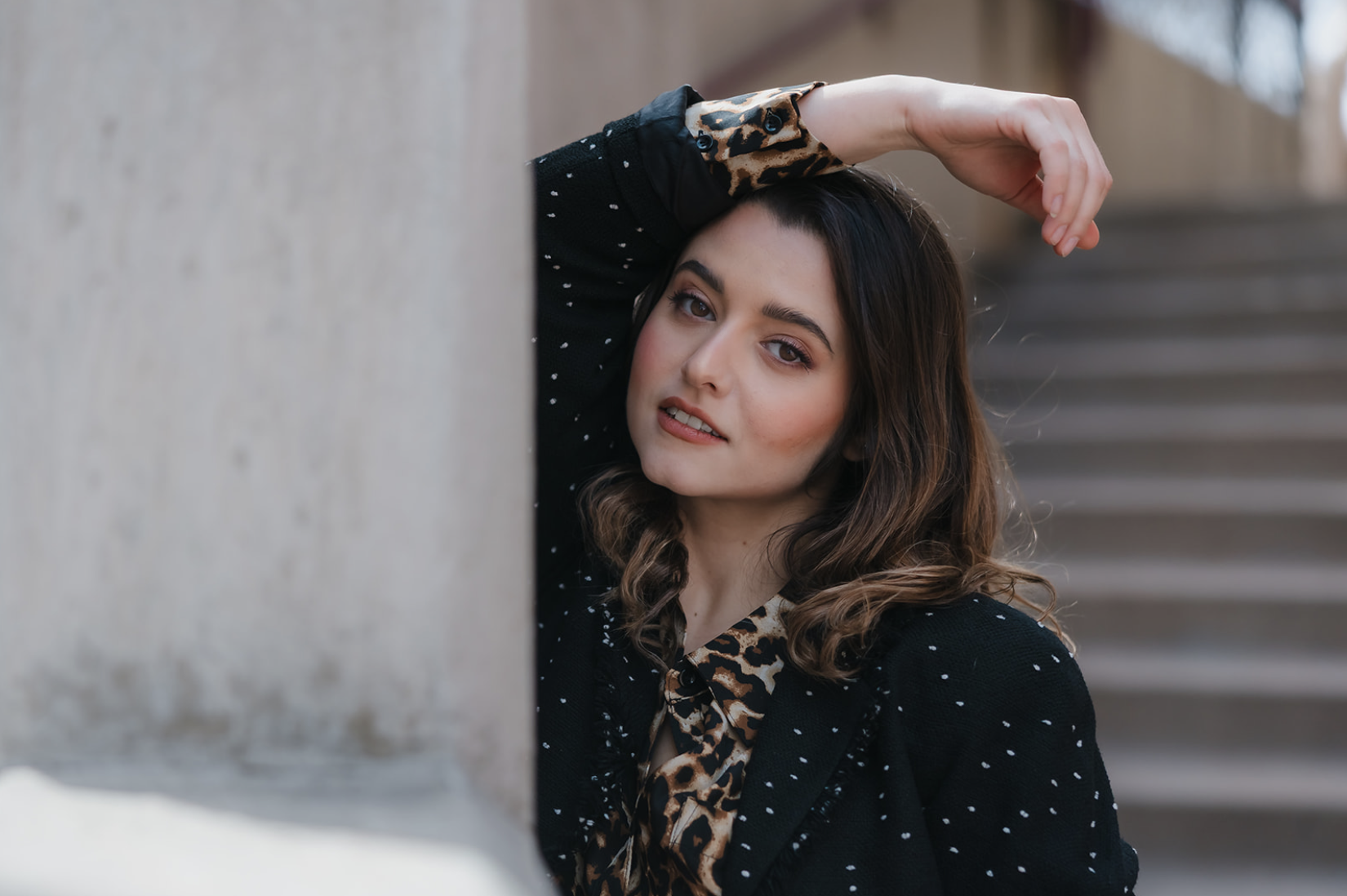 Black and white photo of a man and woman standing outdoors among trees, facing opposite directions with serious expressions, the woman in the foreground and the man slightly behind.